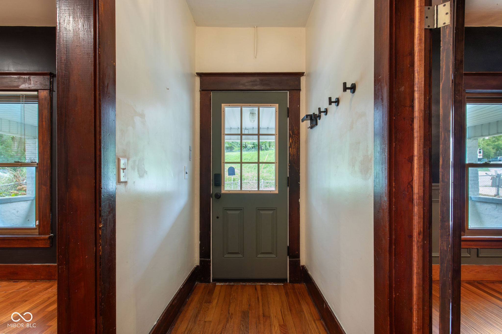Entry hall with a green divided-light front door, dark wood trim, hardwood floors, and coat hooks.