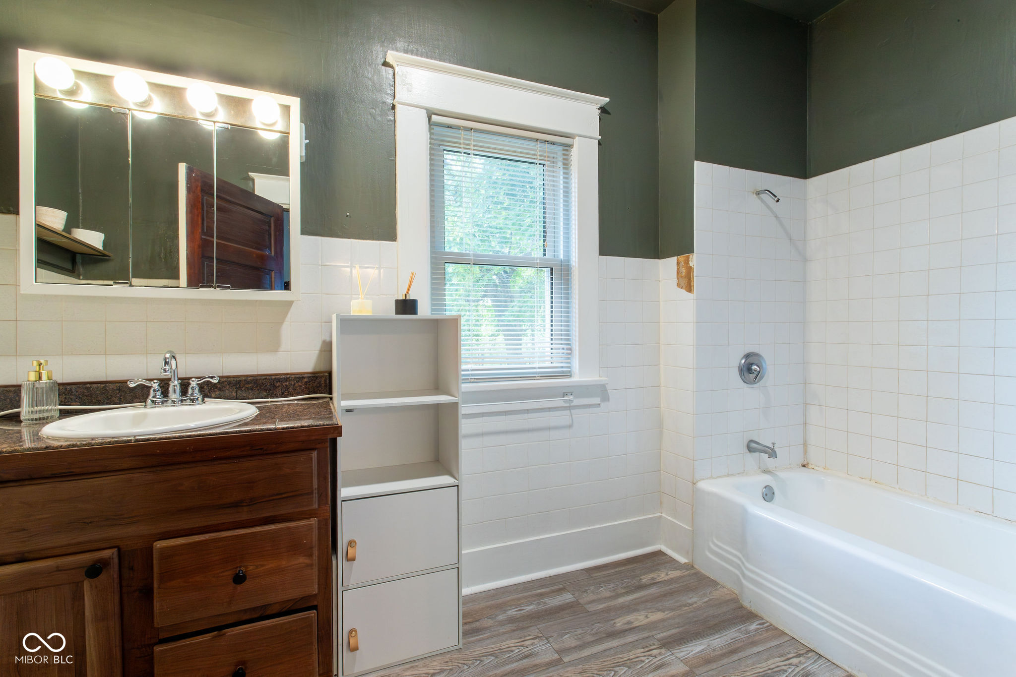 Bathroom with a dark wood vanity, bright mirrored cabinet, window, and white tiled tub and shower.
