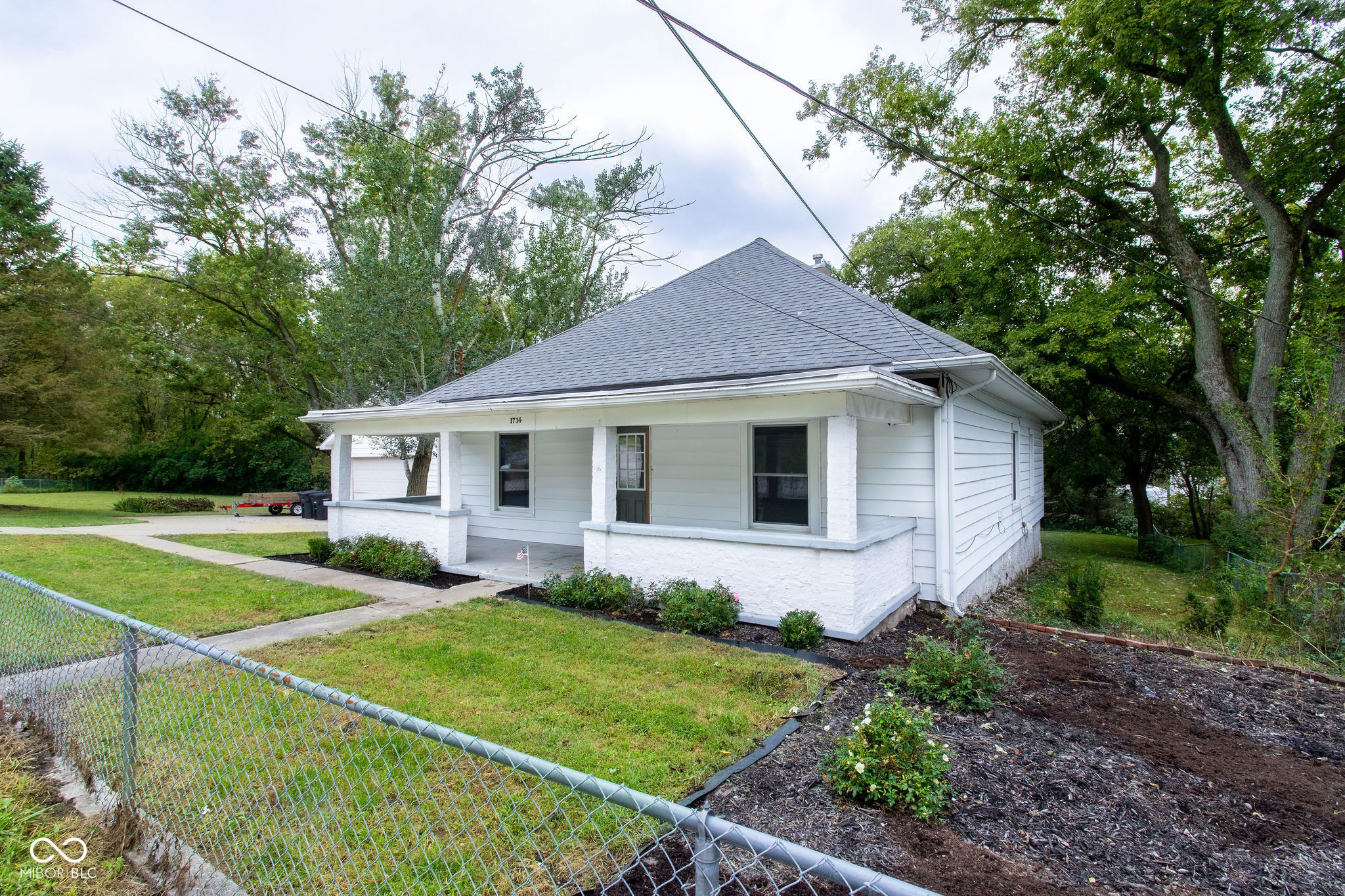 White single-story house with a covered porch, fenced lawn, and mature trees.