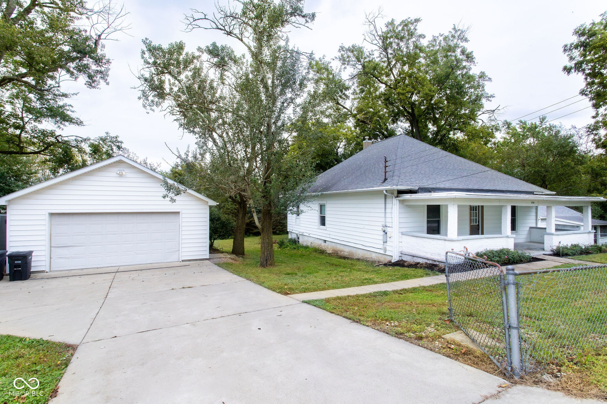 White single-story house with a covered porch, detached garage, and wide concrete driveway.