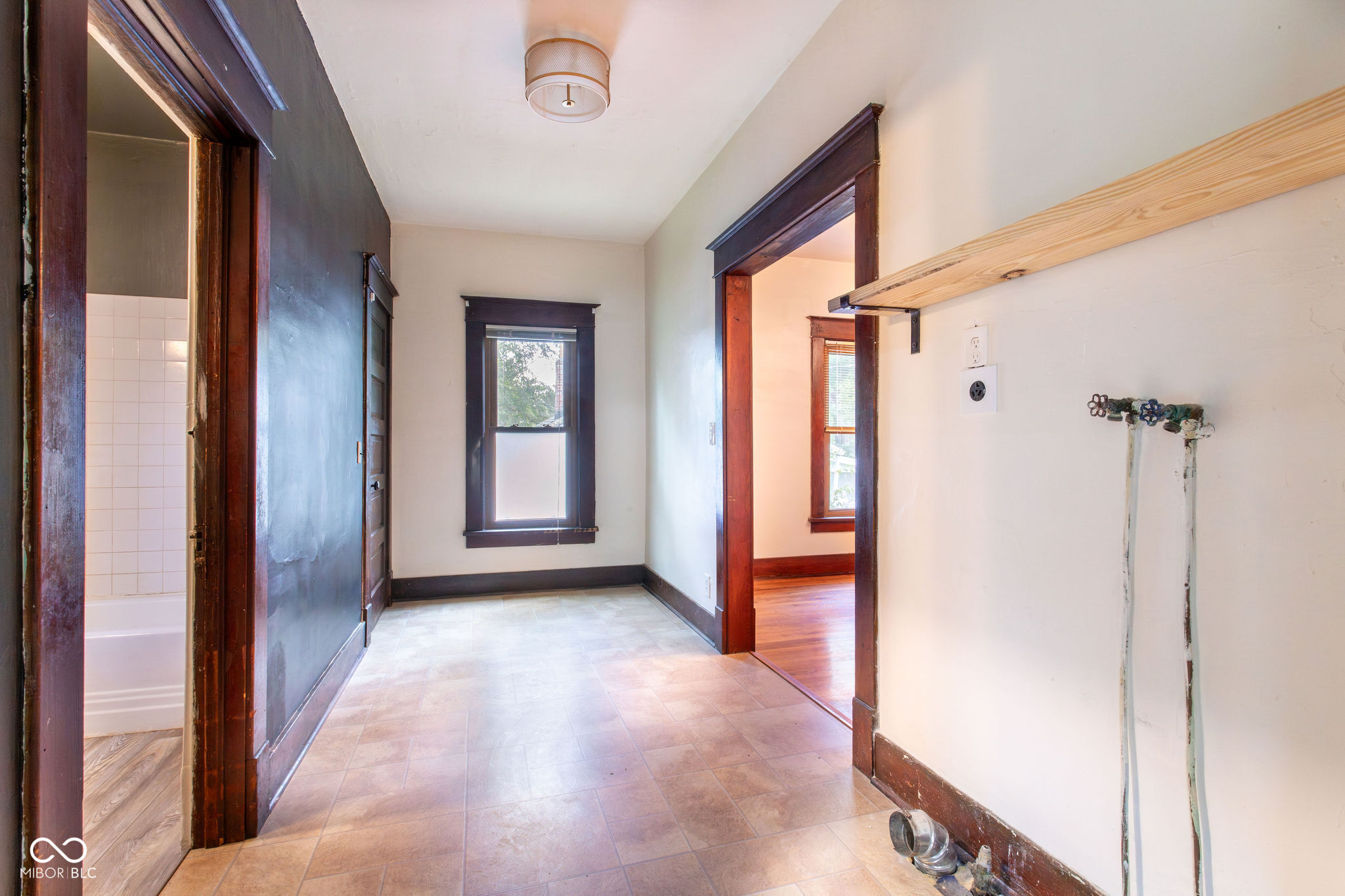 Empty laundry room with tiled floor, exposed washer hookups, and dark wood trim.