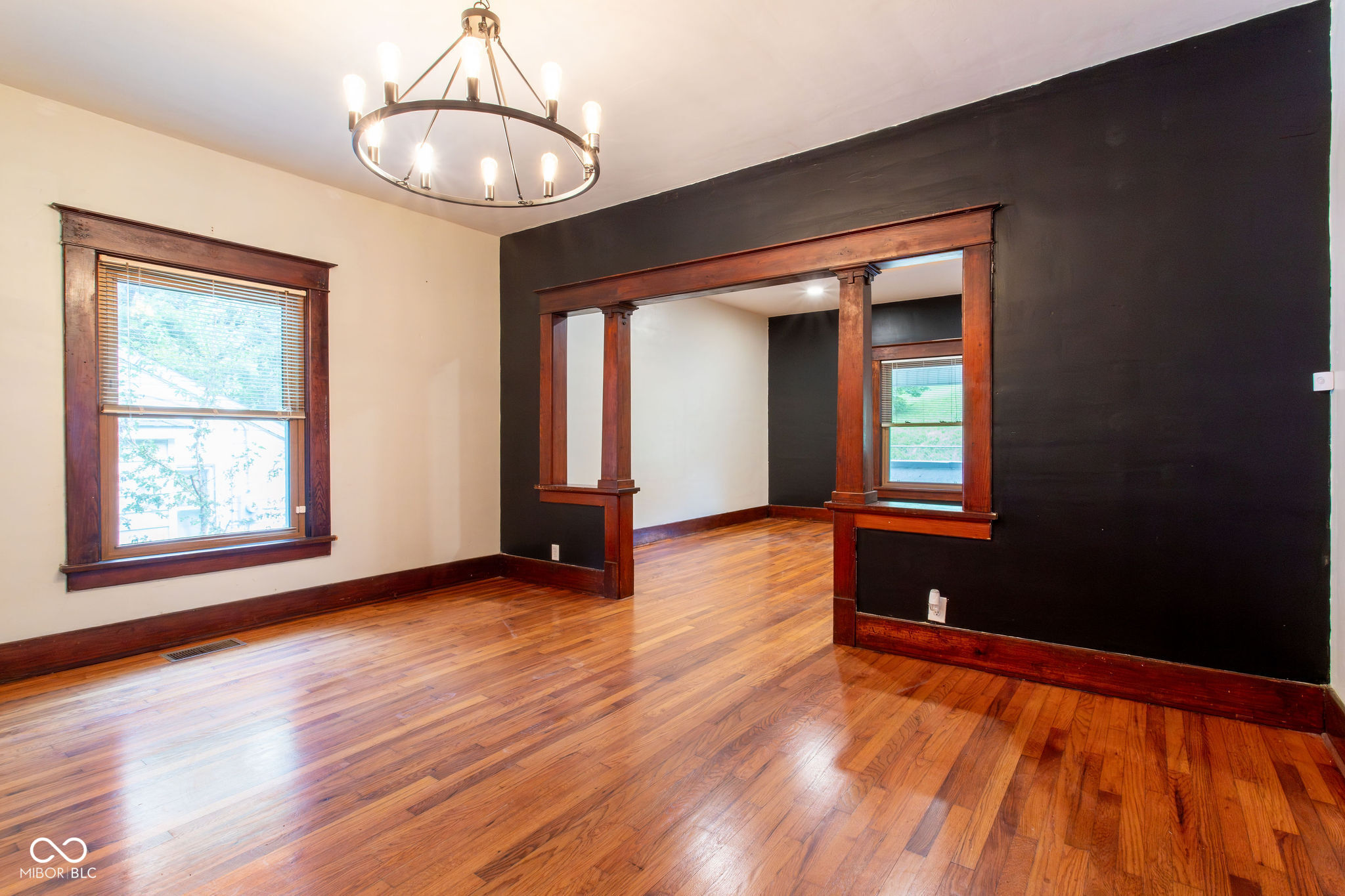 Empty room with polished hardwood floors, dark walls, and ornate stained-wood trim.