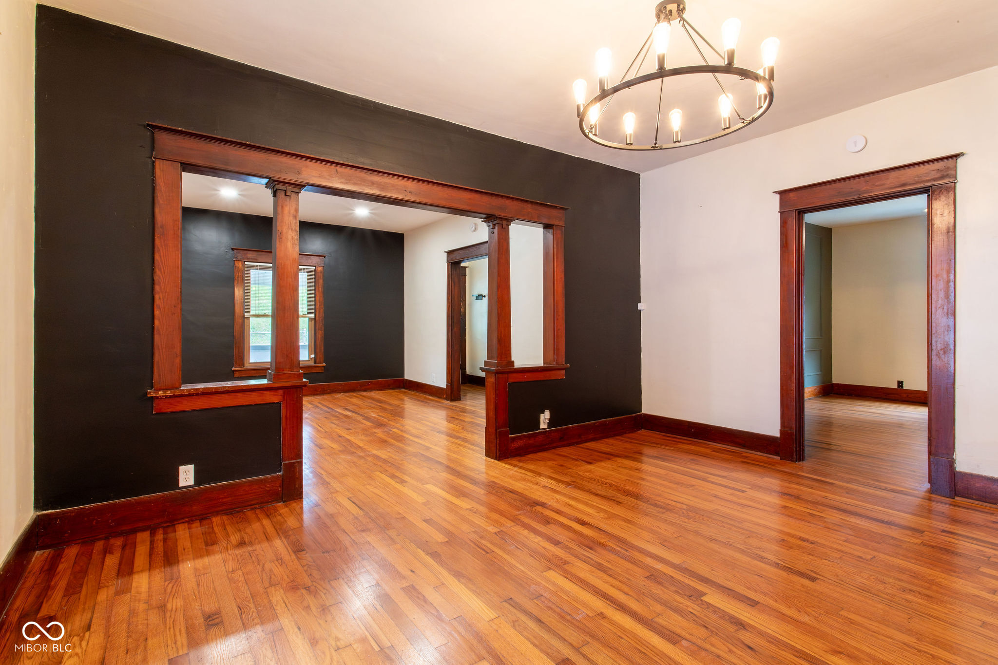 Vacant room with hardwood floors, dark accent wall, ornate wood trim, and a circular chandelier.