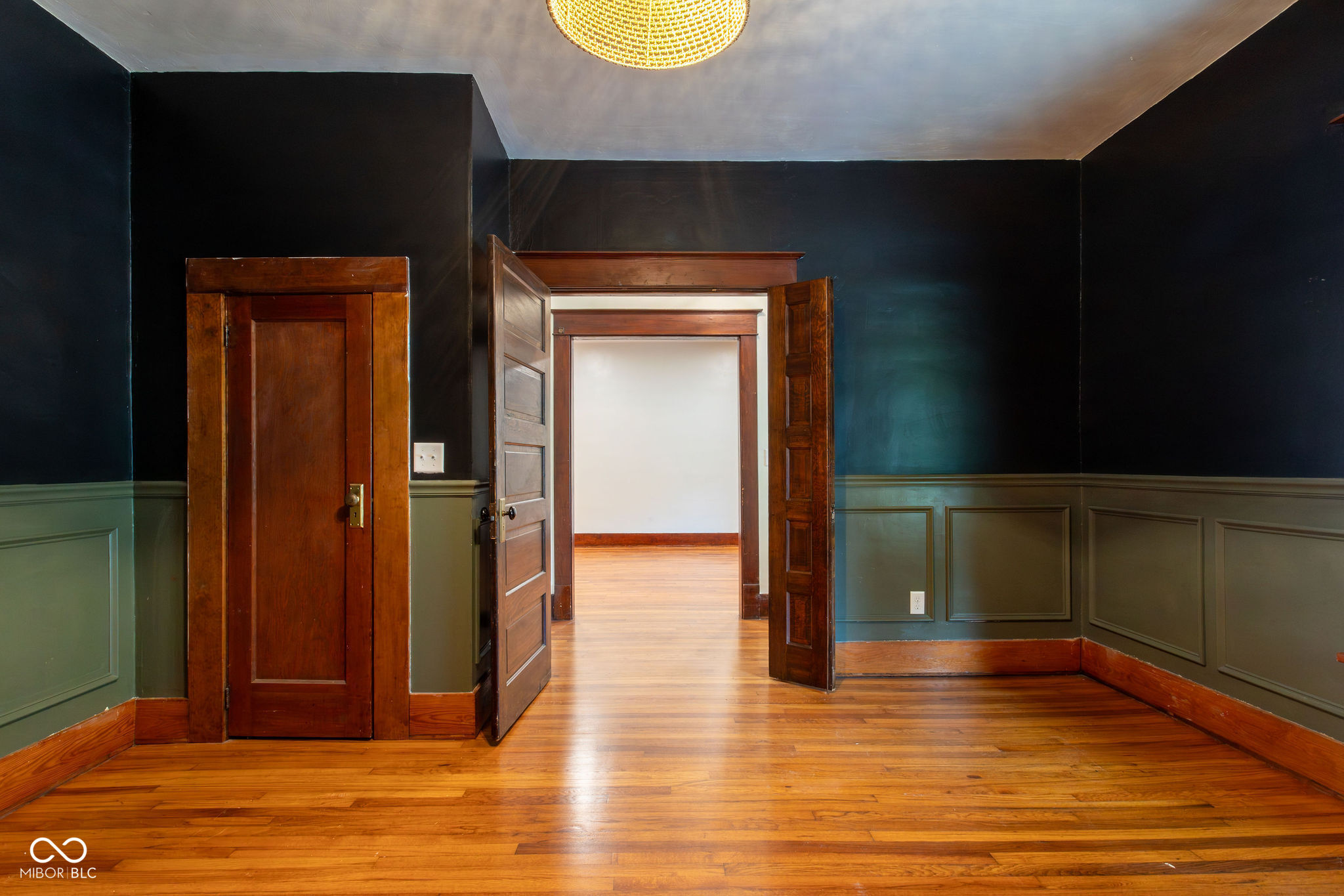 Vacant room with hardwood floors, paneled wainscoting, and open dark wood doors.