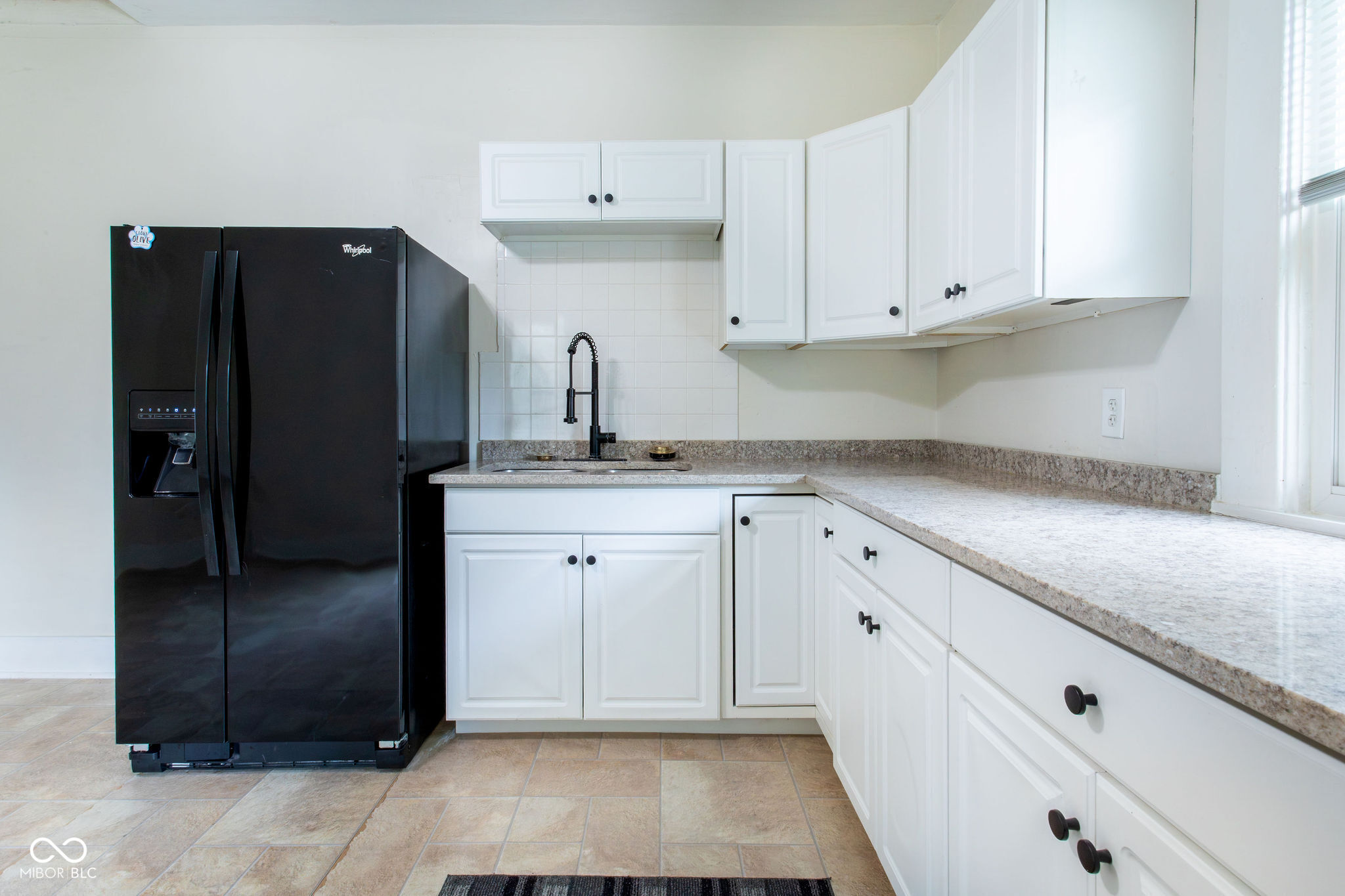Kitchen with white cabinets, stone counters, a black refrigerator, and a tall spring-coil faucet.