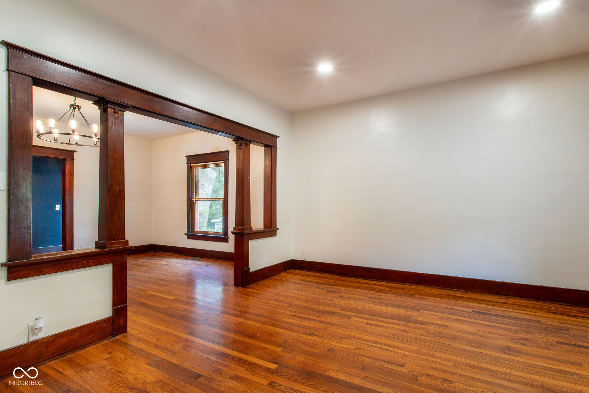 Empty room with polished hardwood floors and dark wood trim framing an opening to an adjoining room.