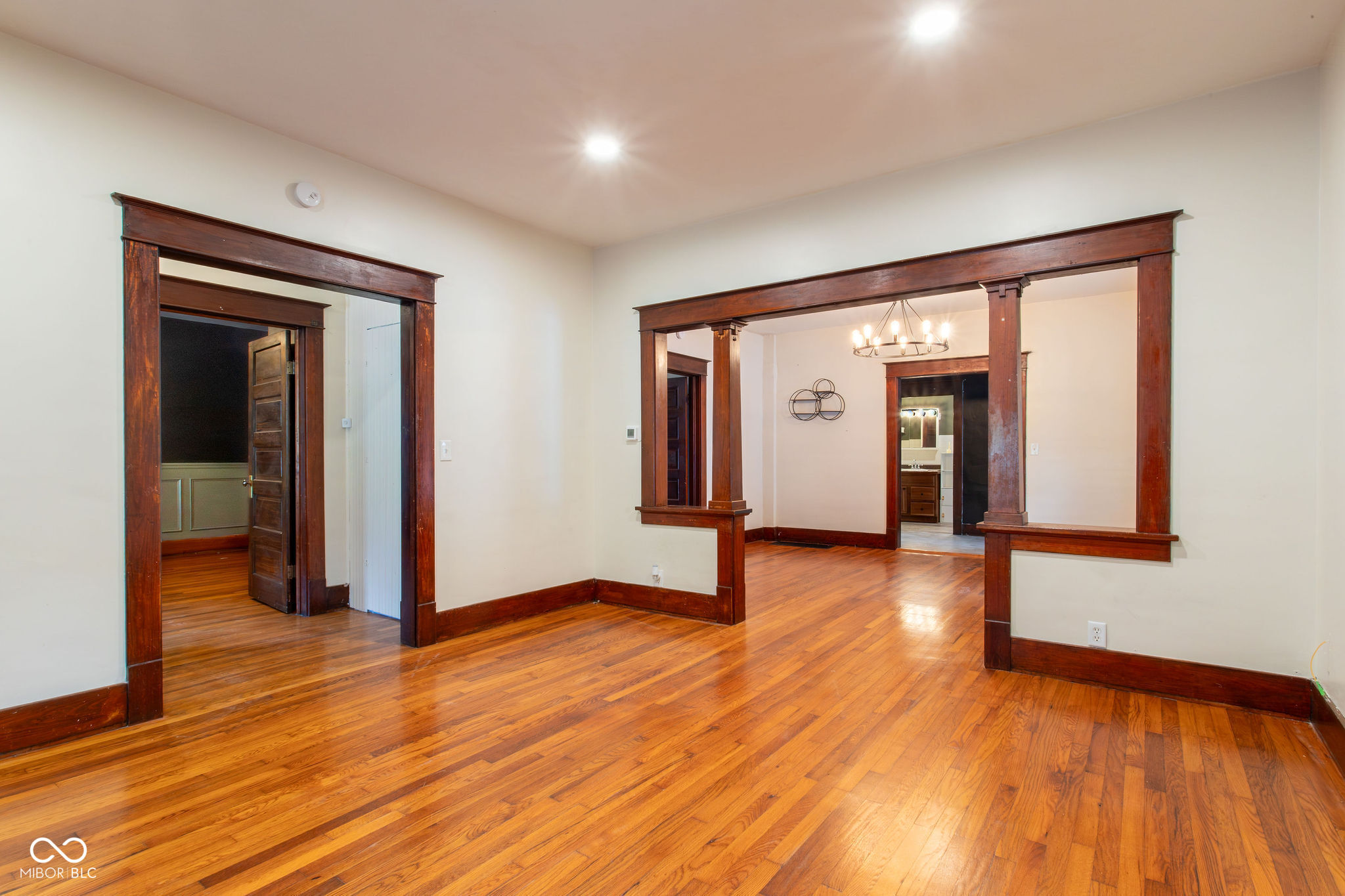 Empty room with polished hardwood floors and wide, dark wood-trimmed openings to adjoining rooms.