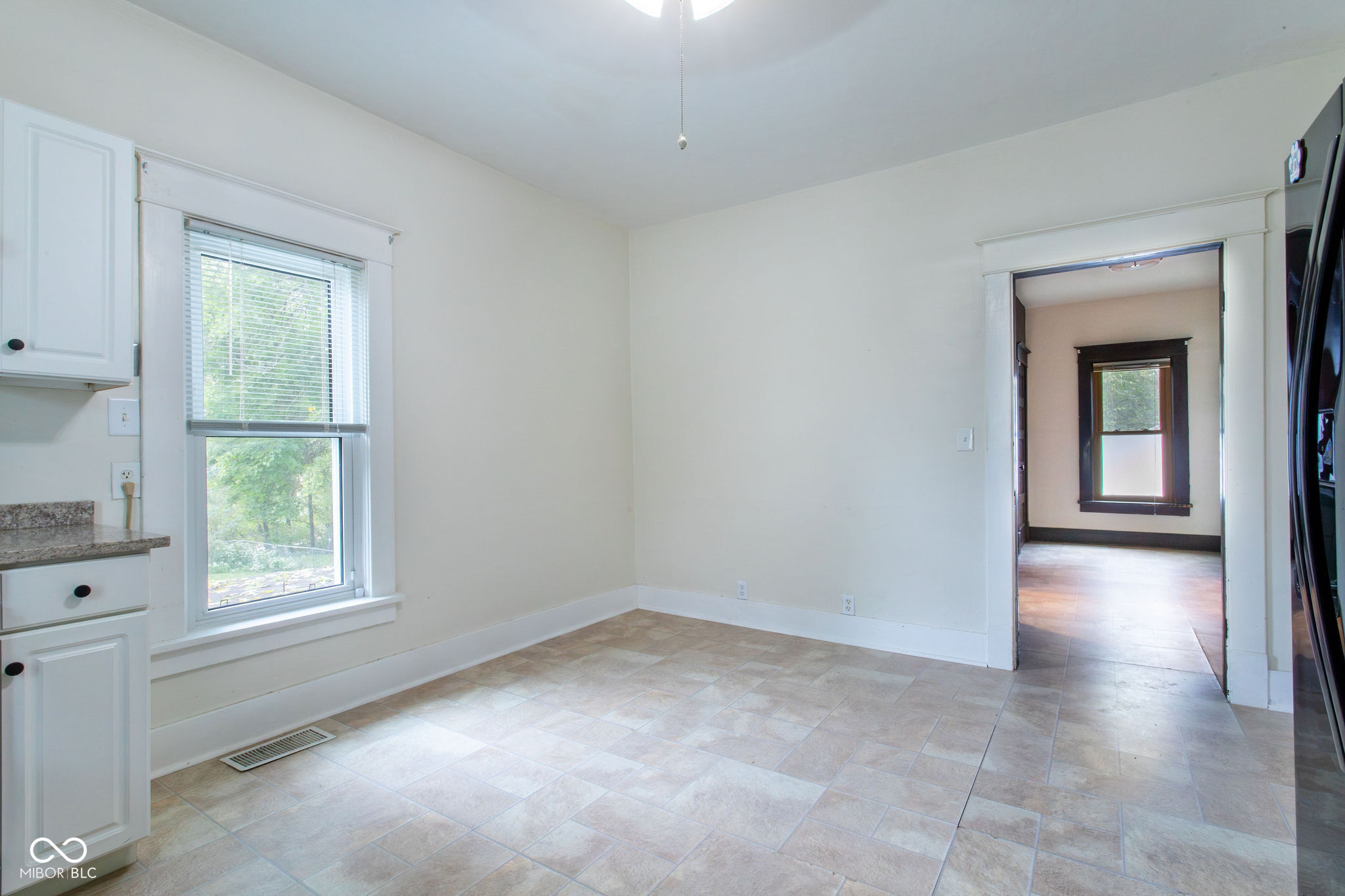 Empty kitchen with white cabinets, beige tile flooring, and a window overlooking greenery.