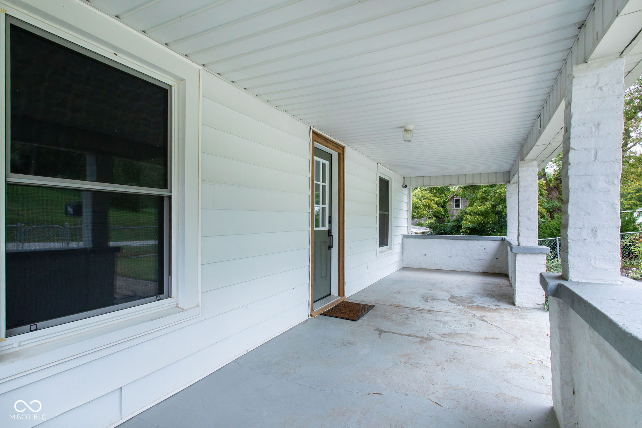 Covered concrete front porch with white columns, a large window, and a dark entry door.