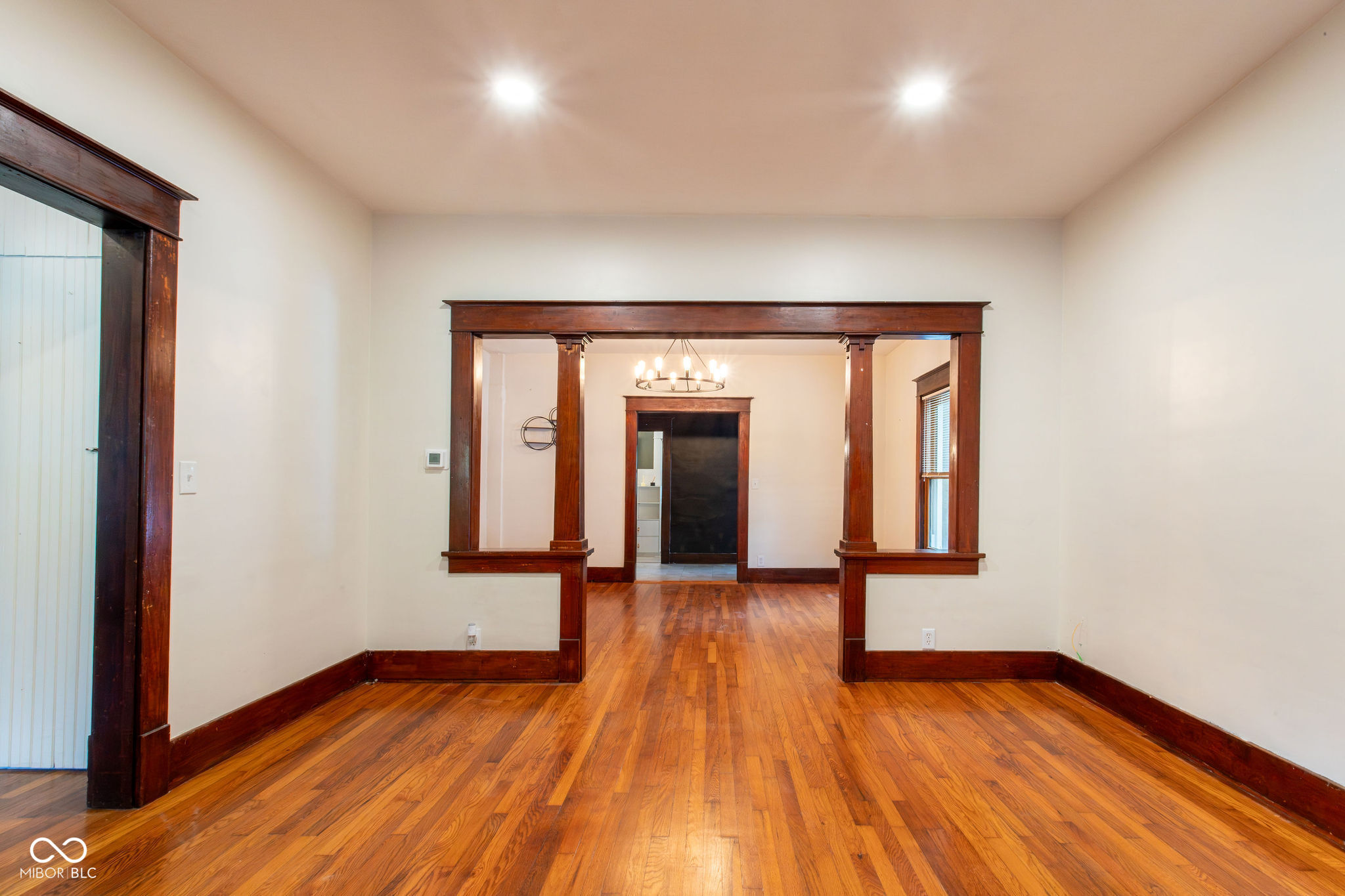 Empty room with polished hardwood floors and dark wood trim framing an opening to the adjoining room.