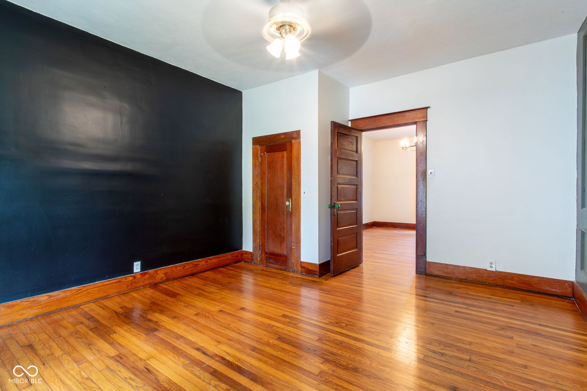 Empty room with polished hardwood floors, a black accent wall, and an open dark wood doorway.