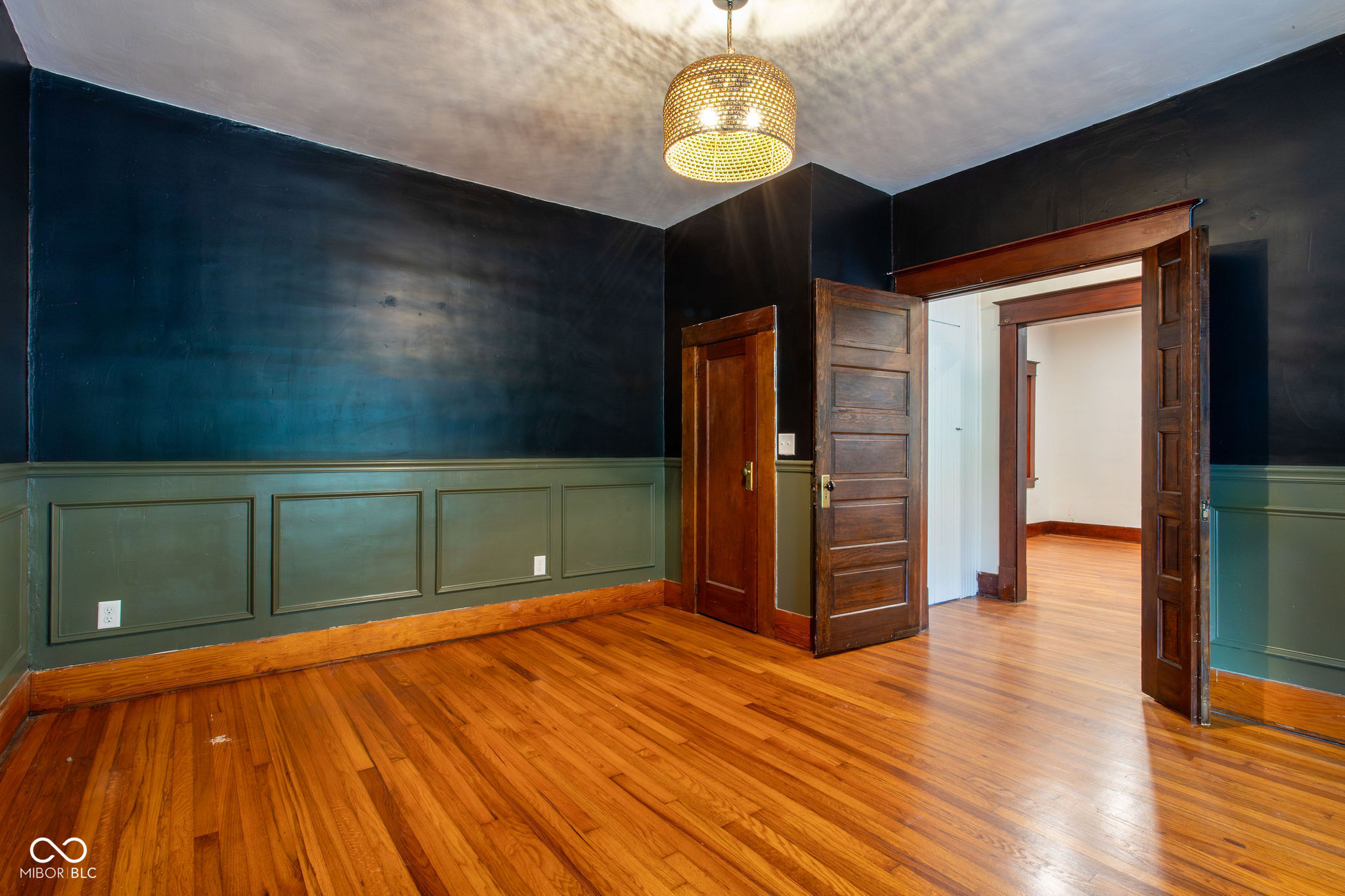 Empty room with polished hardwood floors, dark walls, paneled wainscoting, and open wooden doors.
