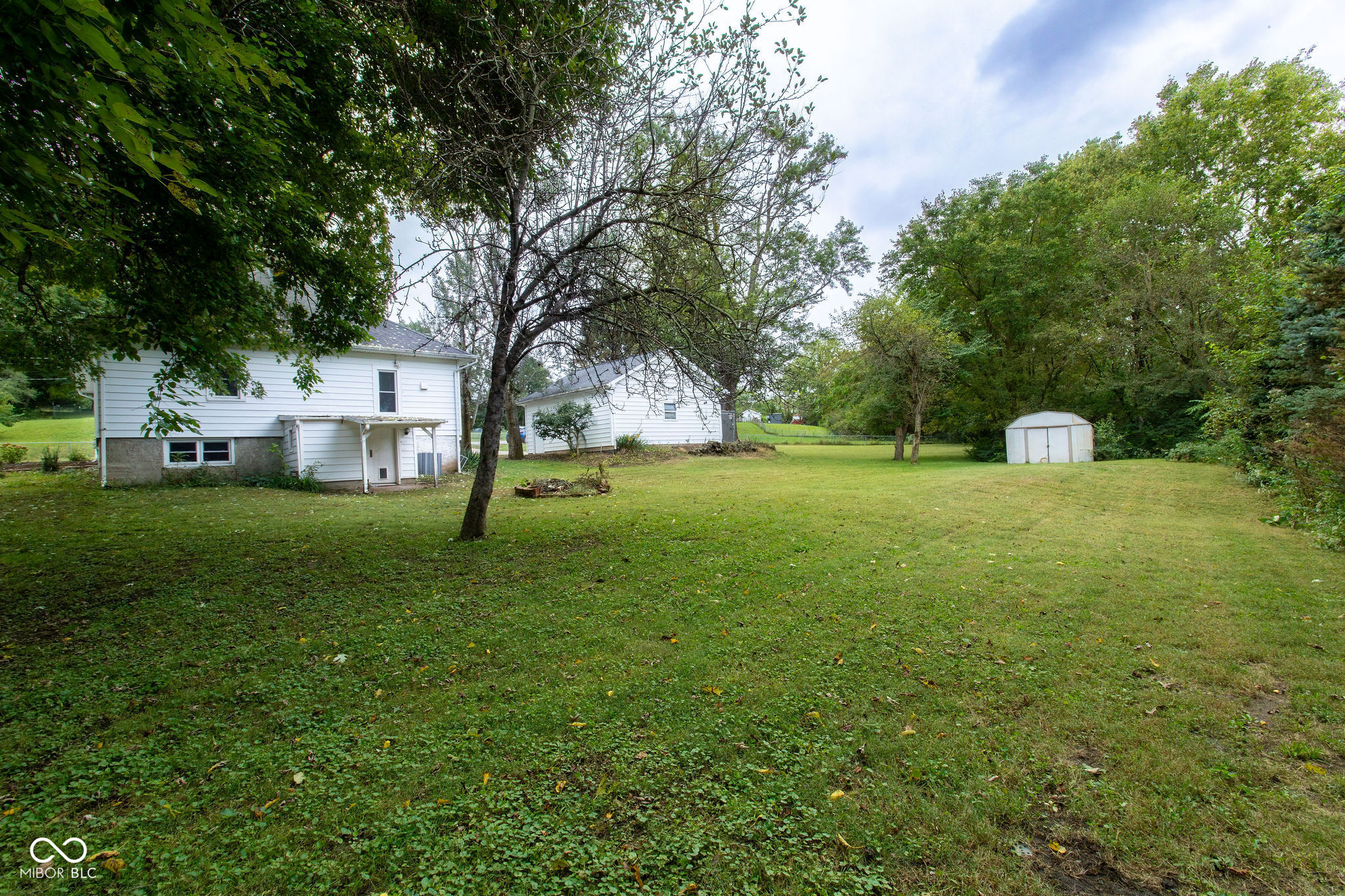White-sided house and outbuildings beyond a broad lawn with mature trees.