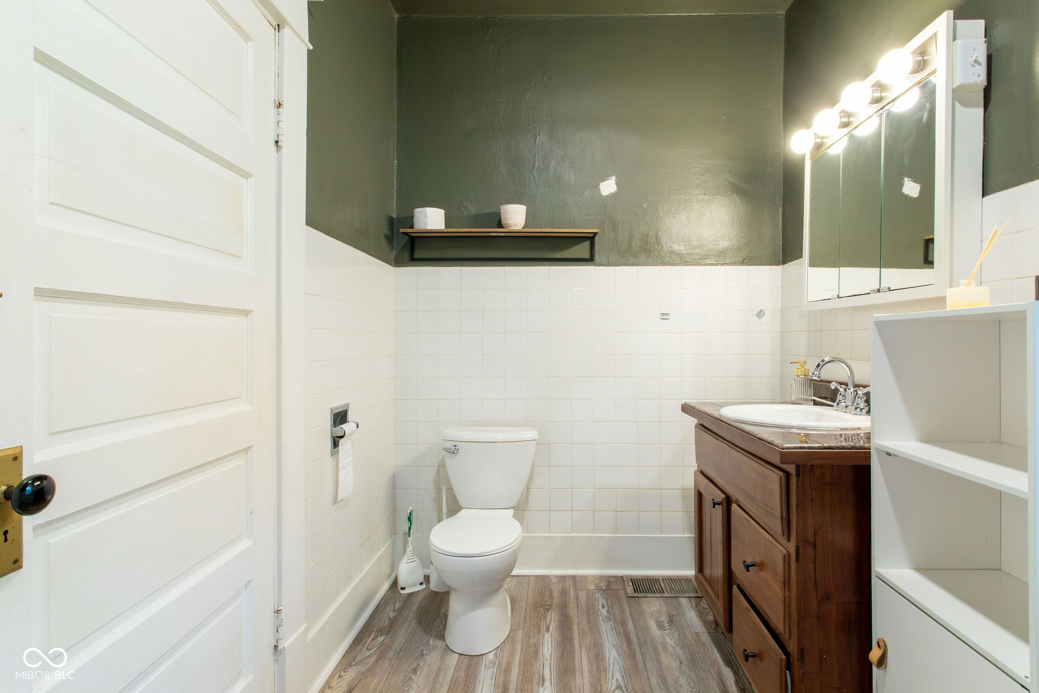 Bathroom with tiled walls, toilet, dark wood vanity, mirrored cabinet, and wood-look flooring.