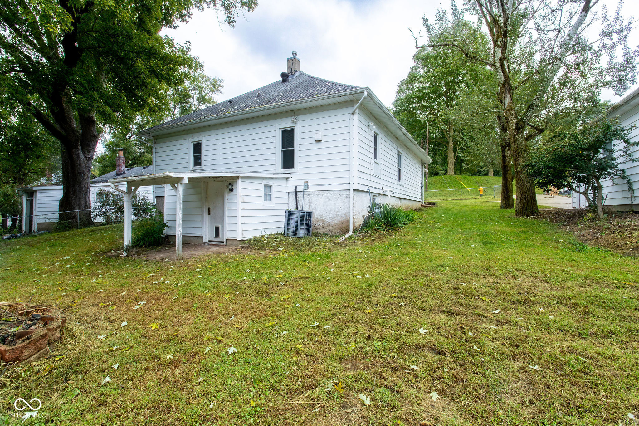 White two-story house viewed from the grassy backyard, with a small covered entry and mature trees.