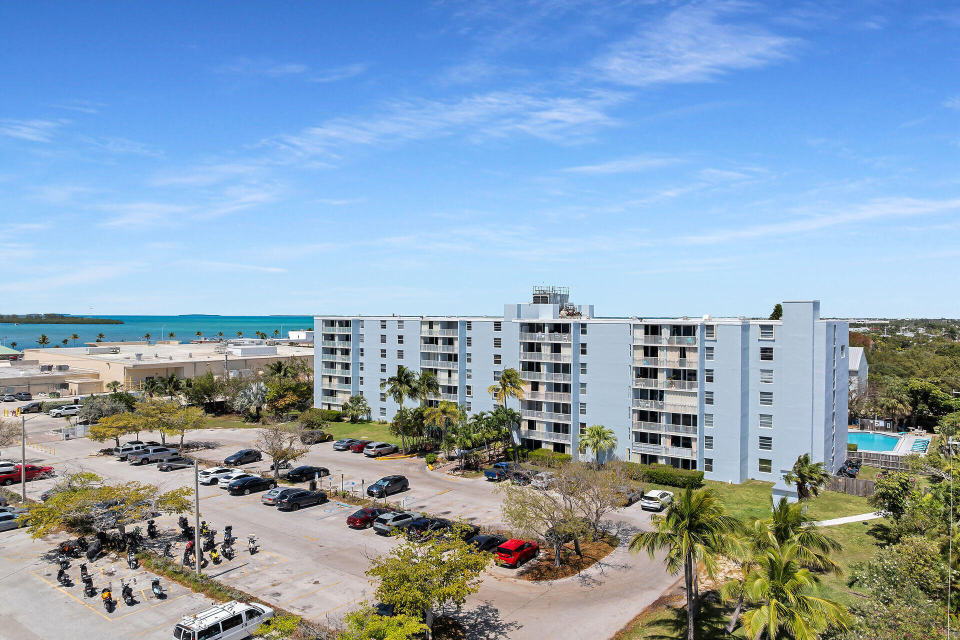 Aerial view of a Key West condominium beside turquoise water, with balconies, palm trees, and a pool.