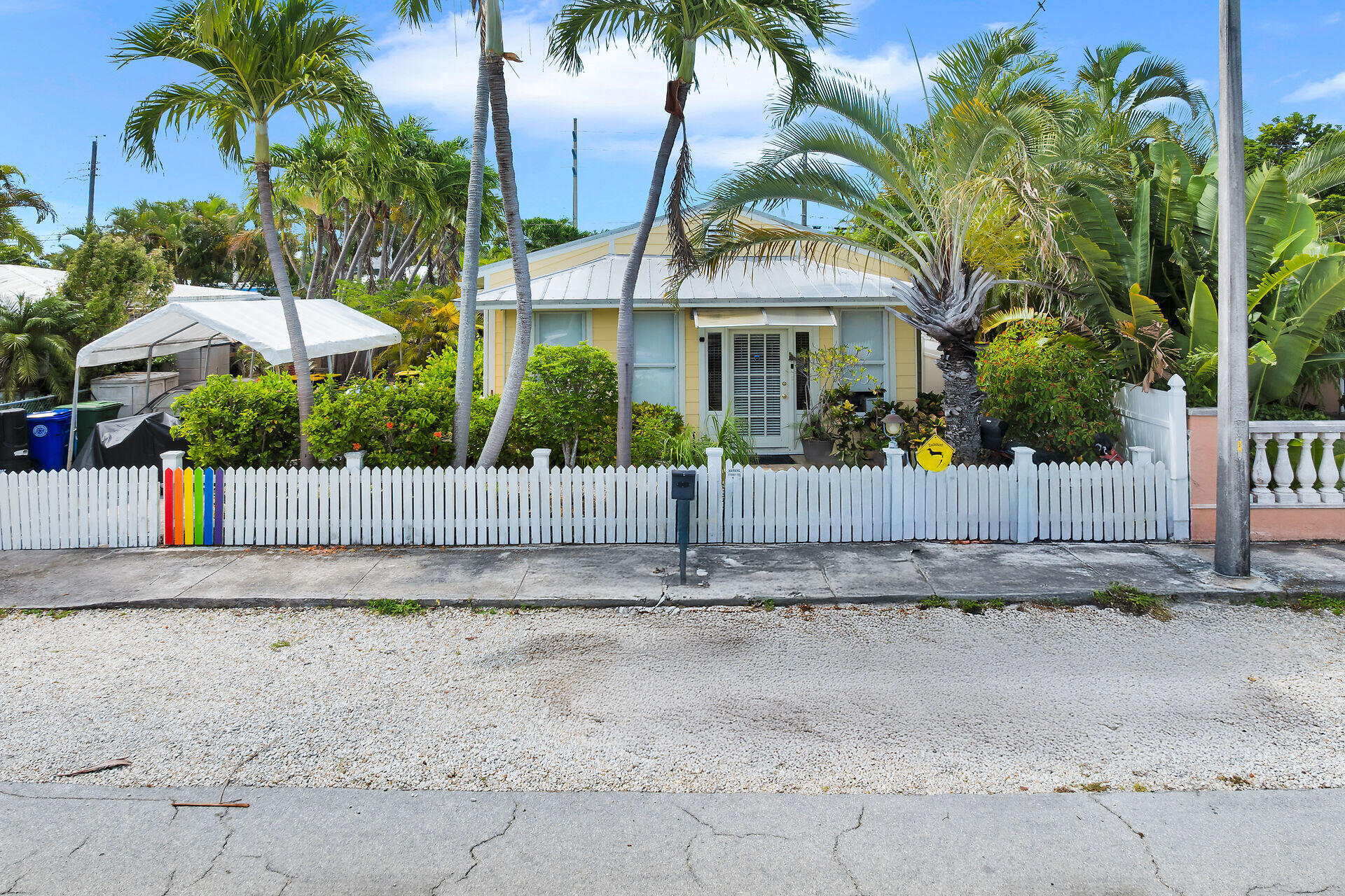 Pale-yellow Key West home behind a white picket fence, framed by palms and tropical landscaping.