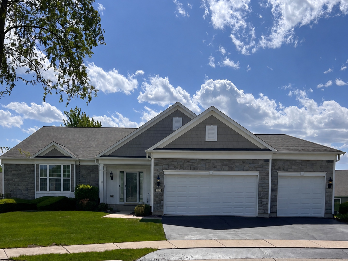 Single-story stone-front home with two garage doors, a gabled roof, and a green lawn.