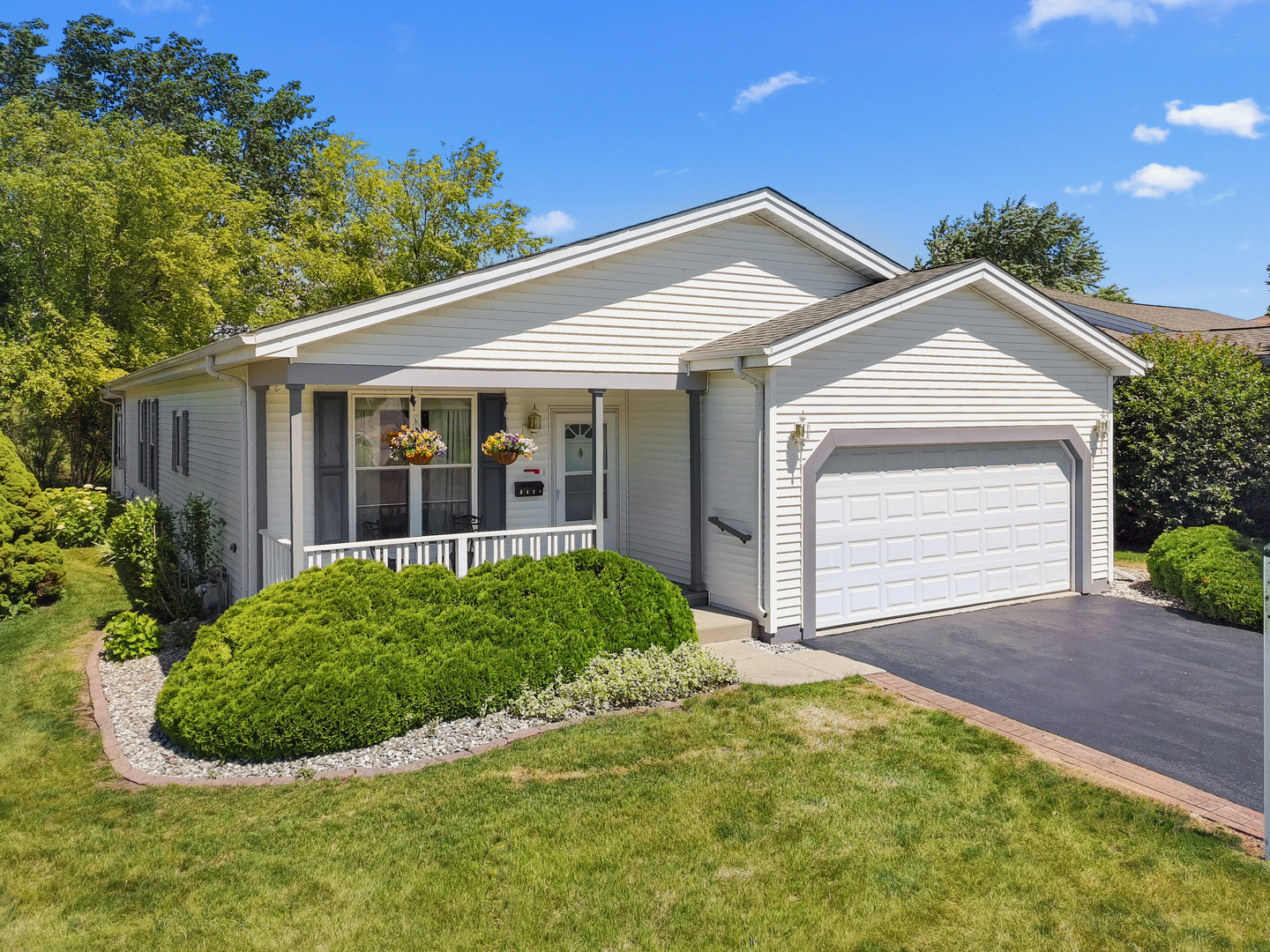 White single-story home with a covered porch, hanging flower baskets, and attached two-car garage.