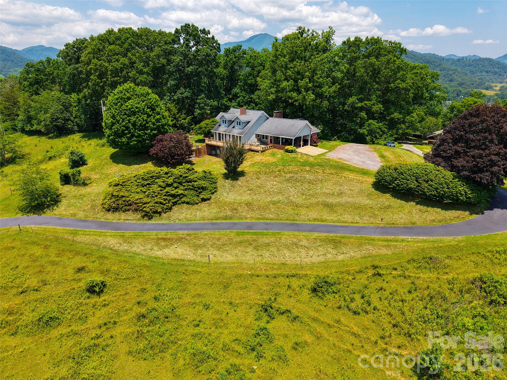 Aerial view of a home on a broad green lawn with wooded mountains behind it.