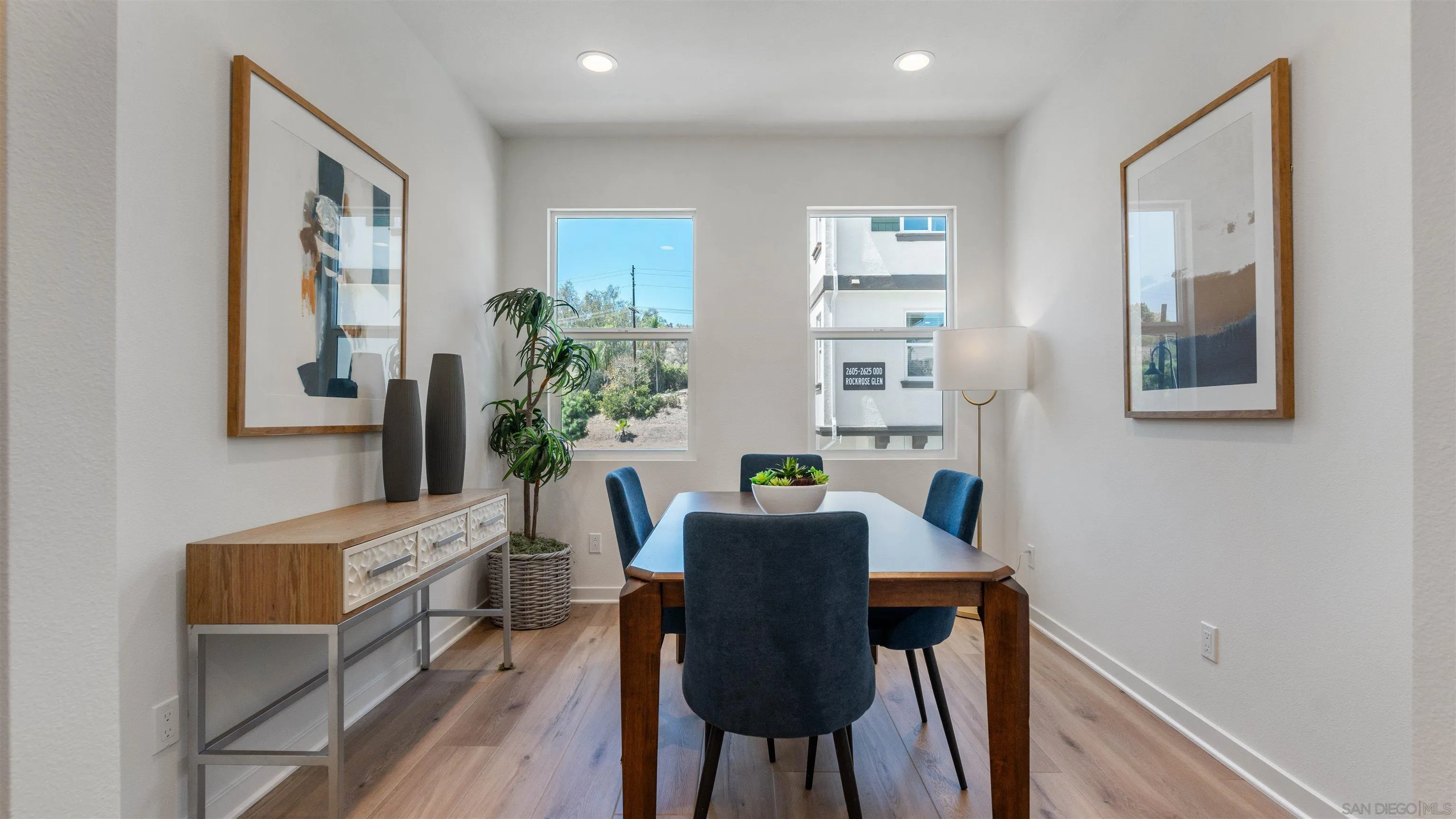 Staged dining room with a wood table, blue chairs, and two bright windows.