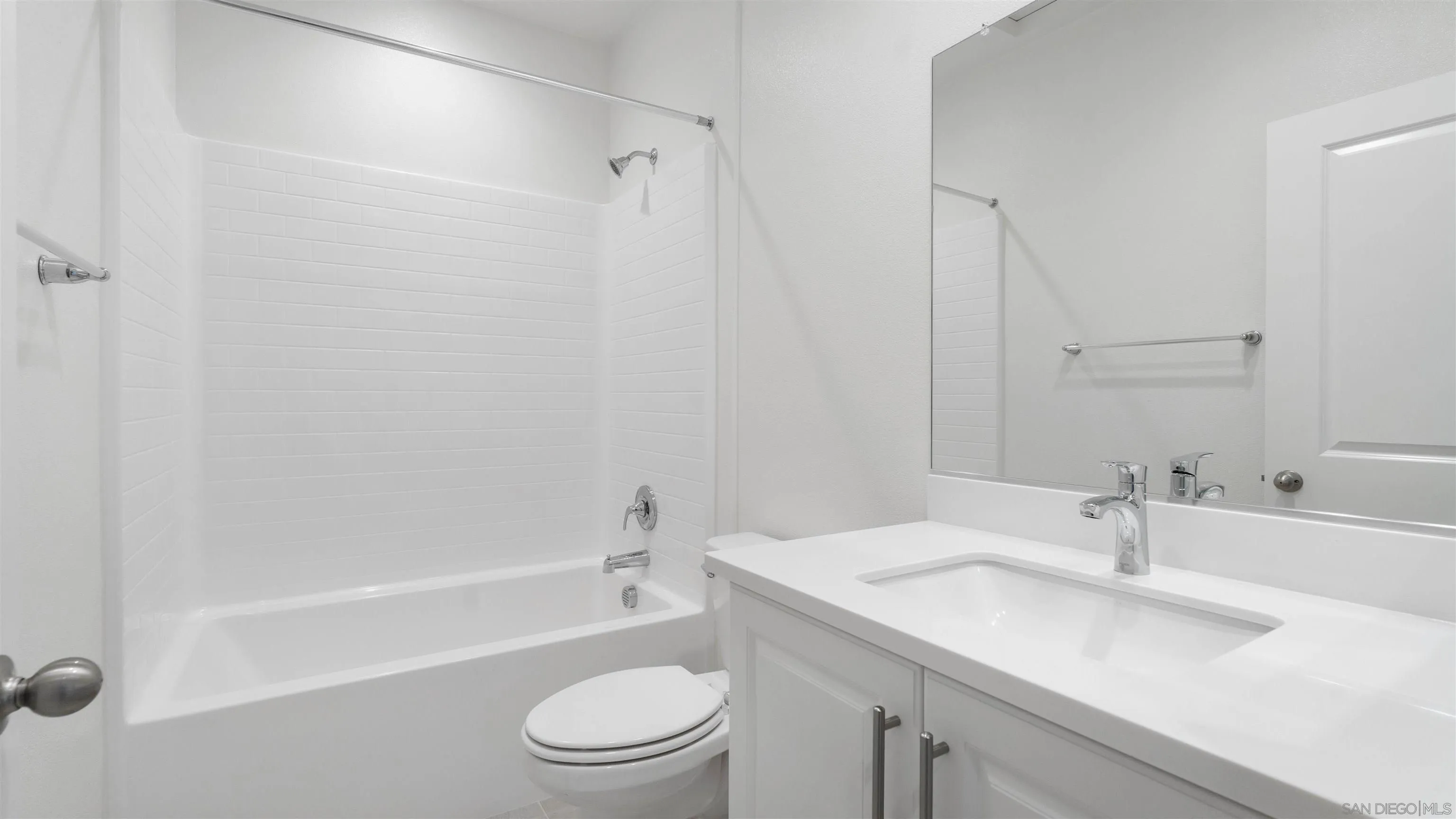 Bathroom with a white tiled bathtub, toilet, and vanity with a large mirror.