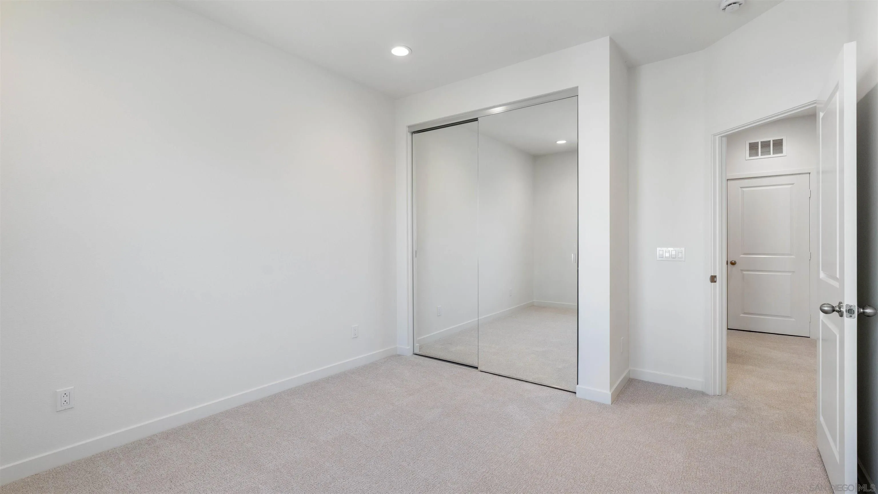 Empty carpeted bedroom with mirrored sliding closet doors and an open doorway.