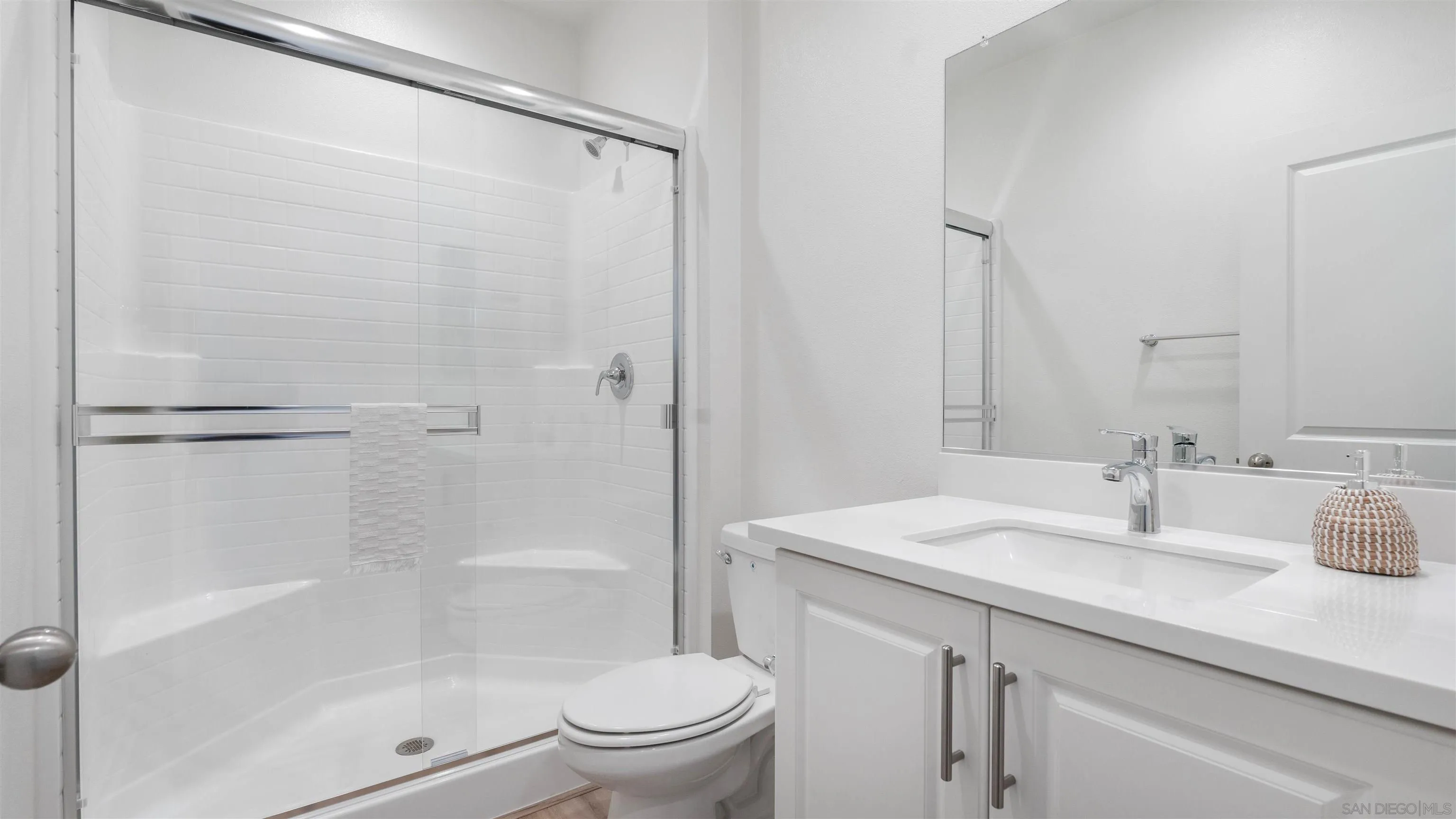 Bright white bathroom with a glass shower, toilet, and vanity with a large mirror.