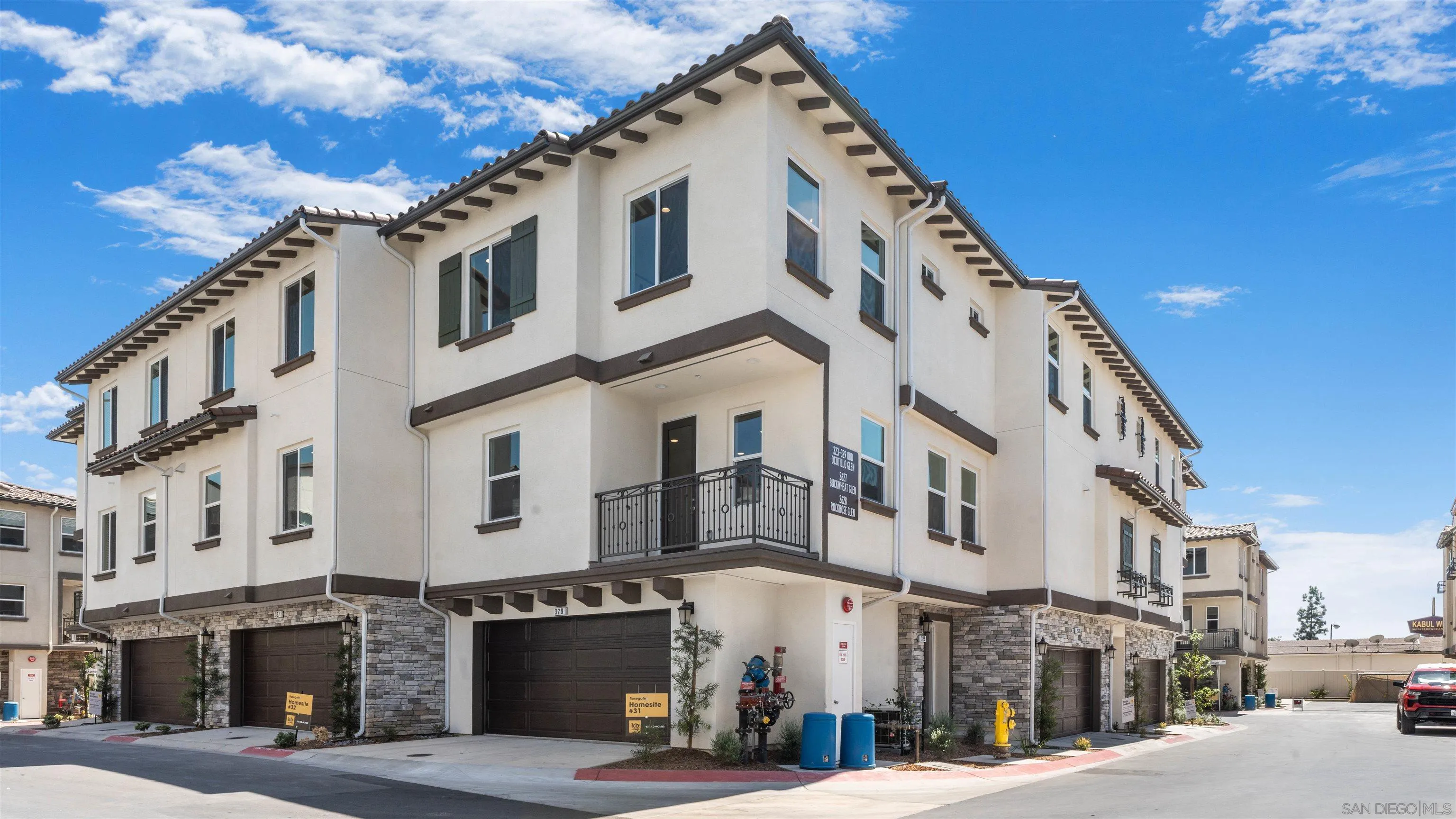 Multi-story townhome with a covered balcony, stone accents, and dark attached garage doors.