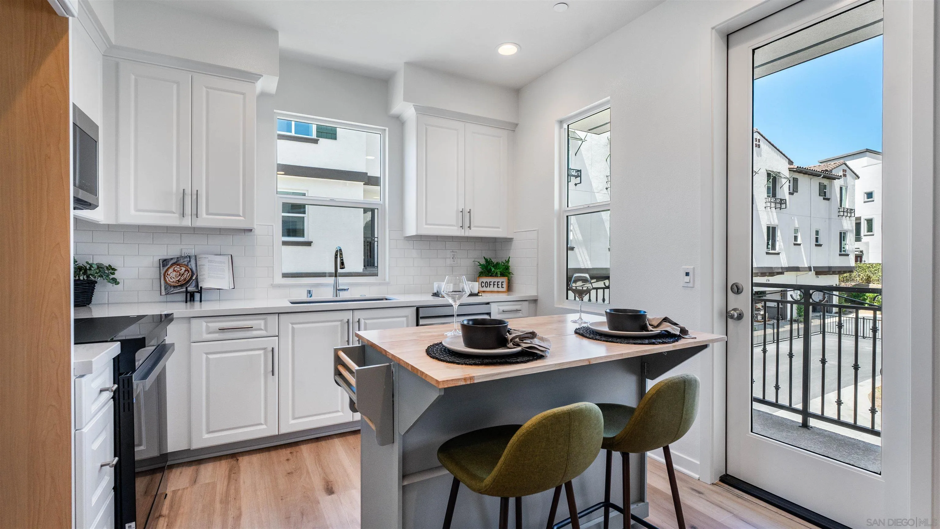 Staged kitchen with a wood-topped island and balcony door overlooking neighboring townhomes.