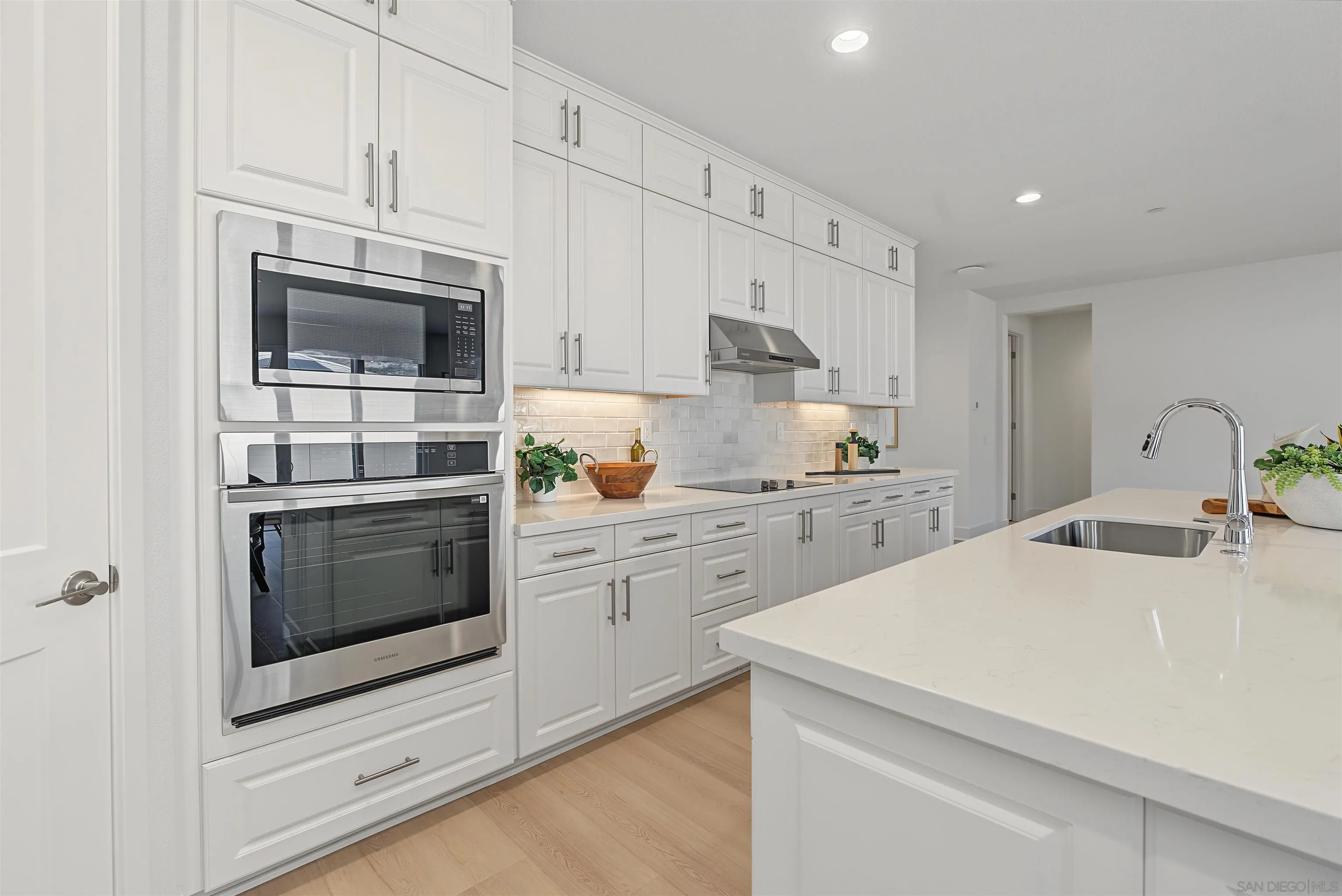 Modern white kitchen with a large island, stainless-steel appliances, and subway-tile backsplash.