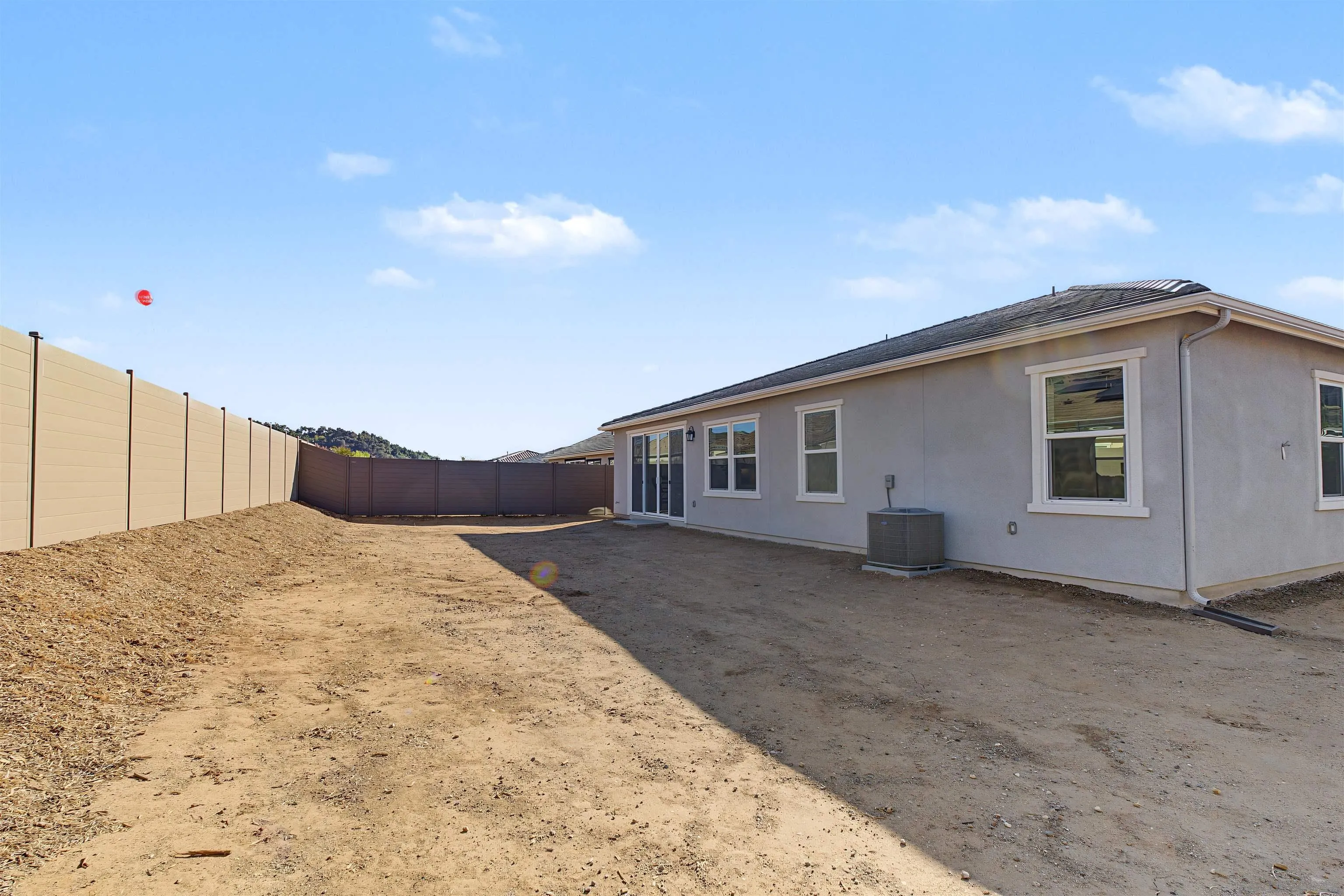 Rear of a single-story home beside a broad dirt backyard enclosed by tall privacy fencing.
