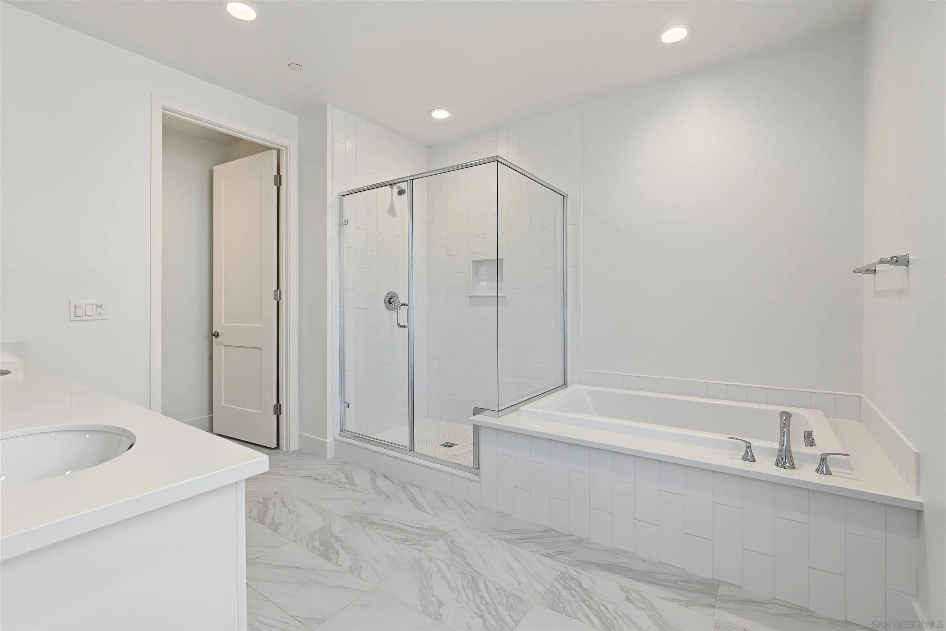 Bright white bathroom with a glass shower, built-in soaking tub, and marble-look tile floor.