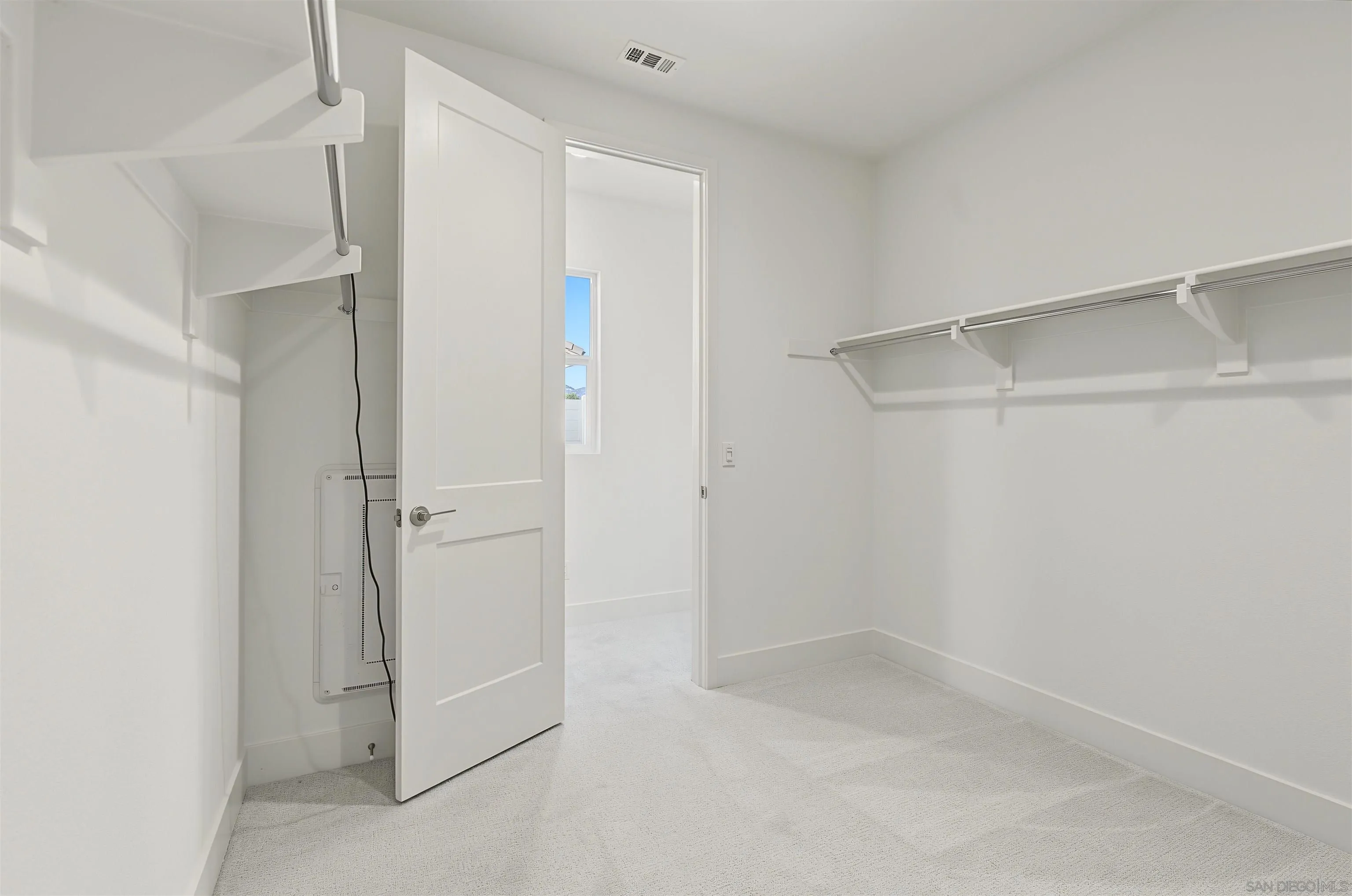 Empty carpeted walk-in closet with built-in shelves and hanging rods.