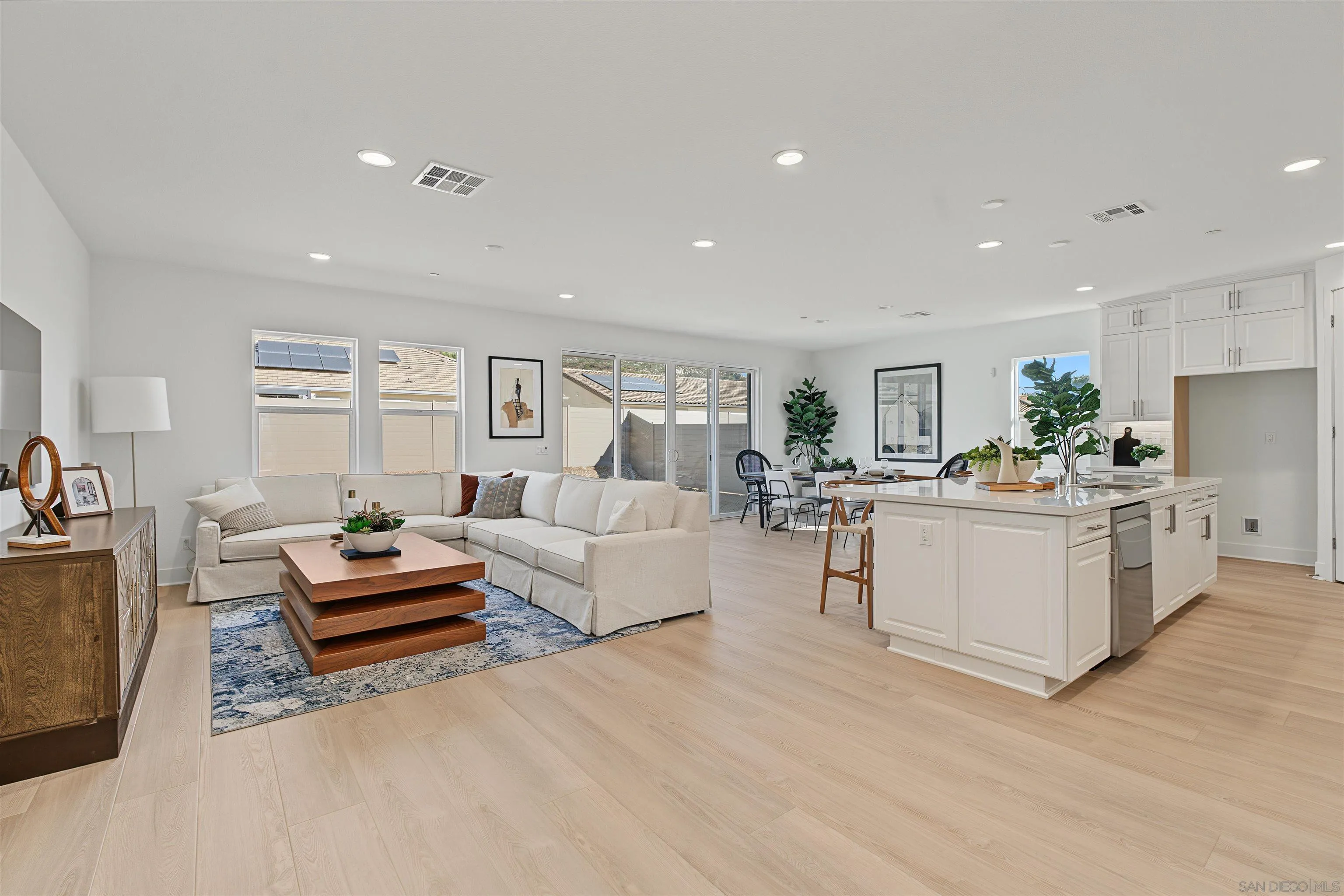 Open-plan living room and kitchen with a white sectional, large island, and pale wood floors.