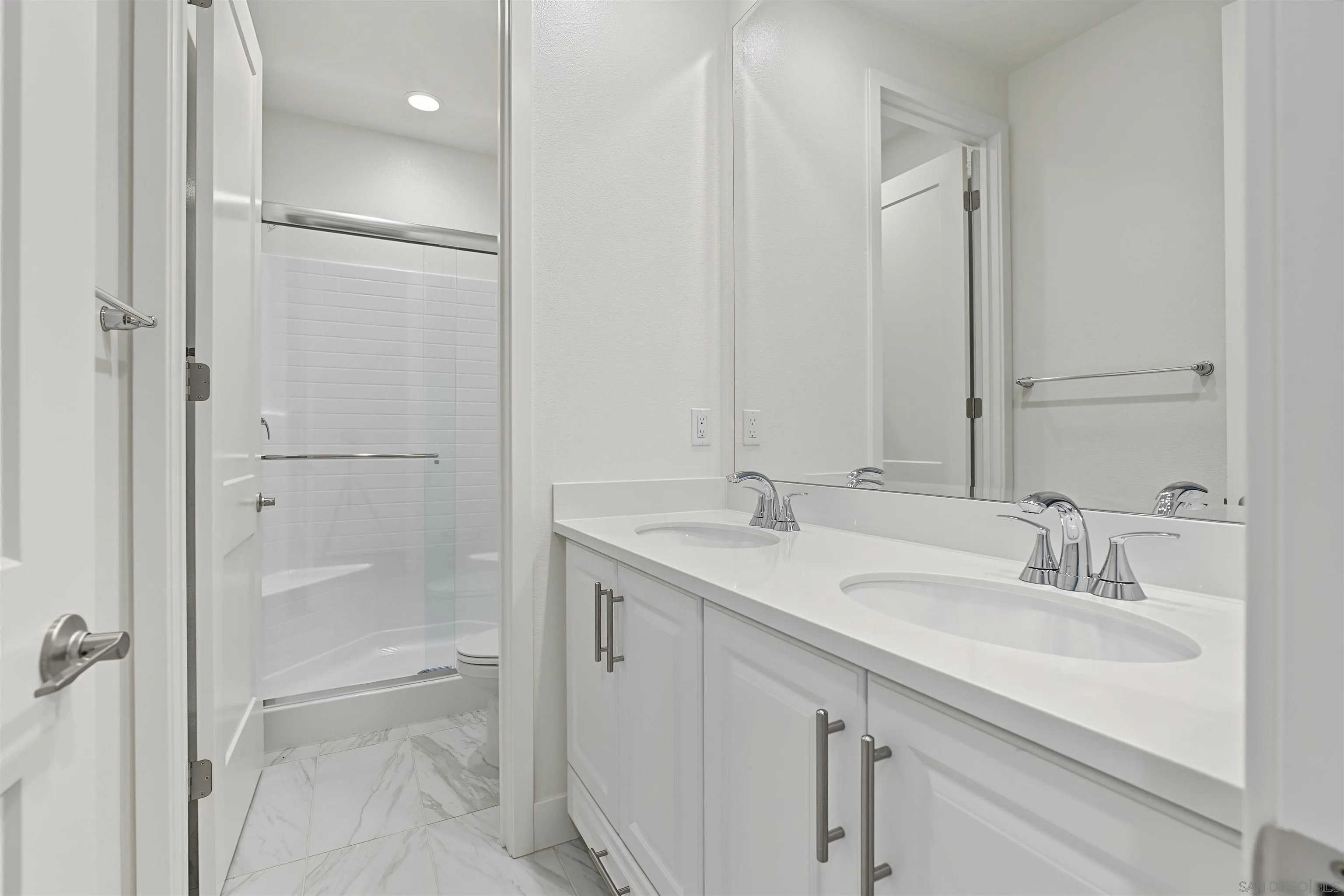 Bathroom with a double-sink white vanity and glass-enclosed tiled shower.