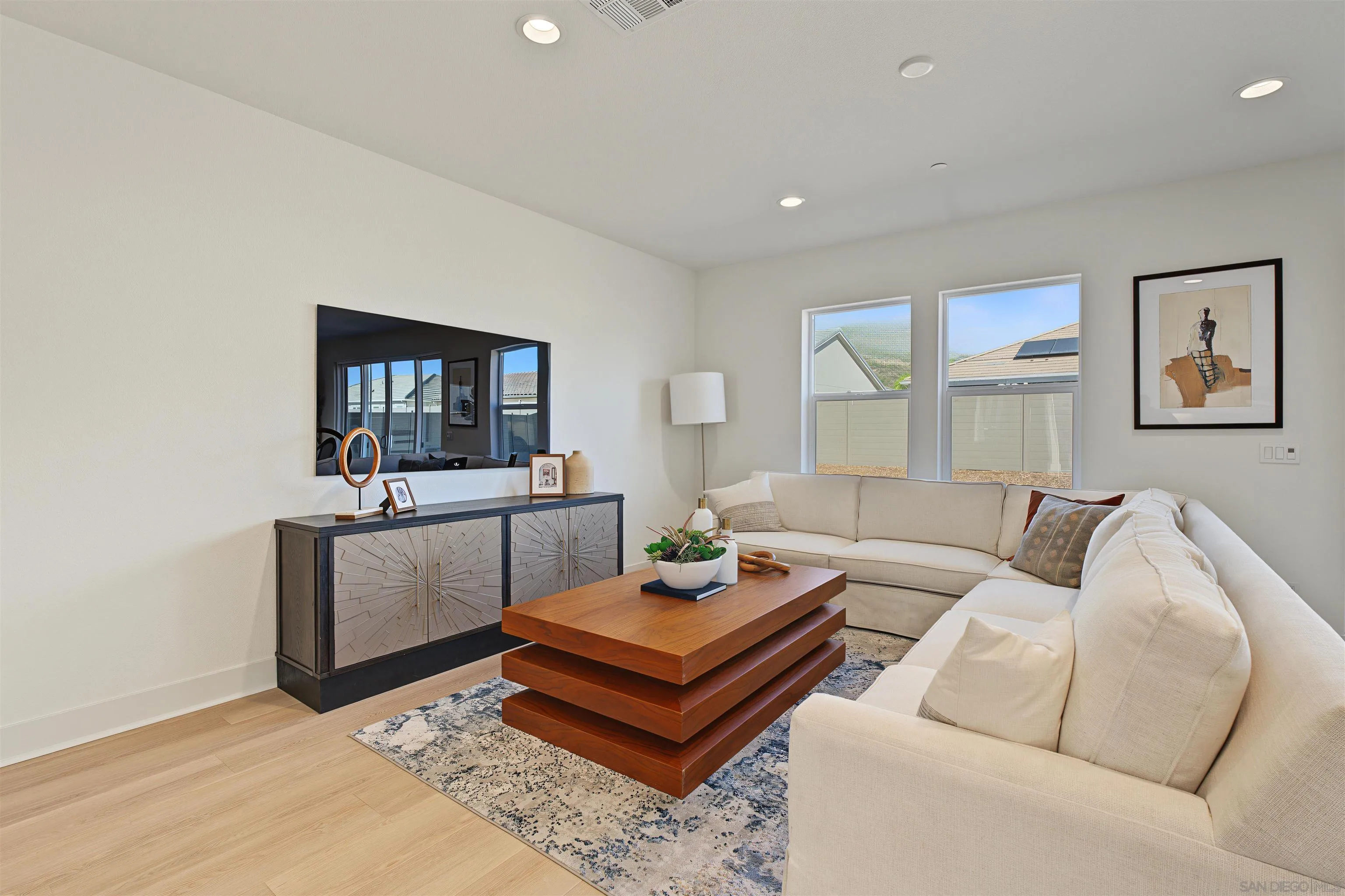 Staged living room with a cream sectional, layered wood coffee table, and large wall mirror.