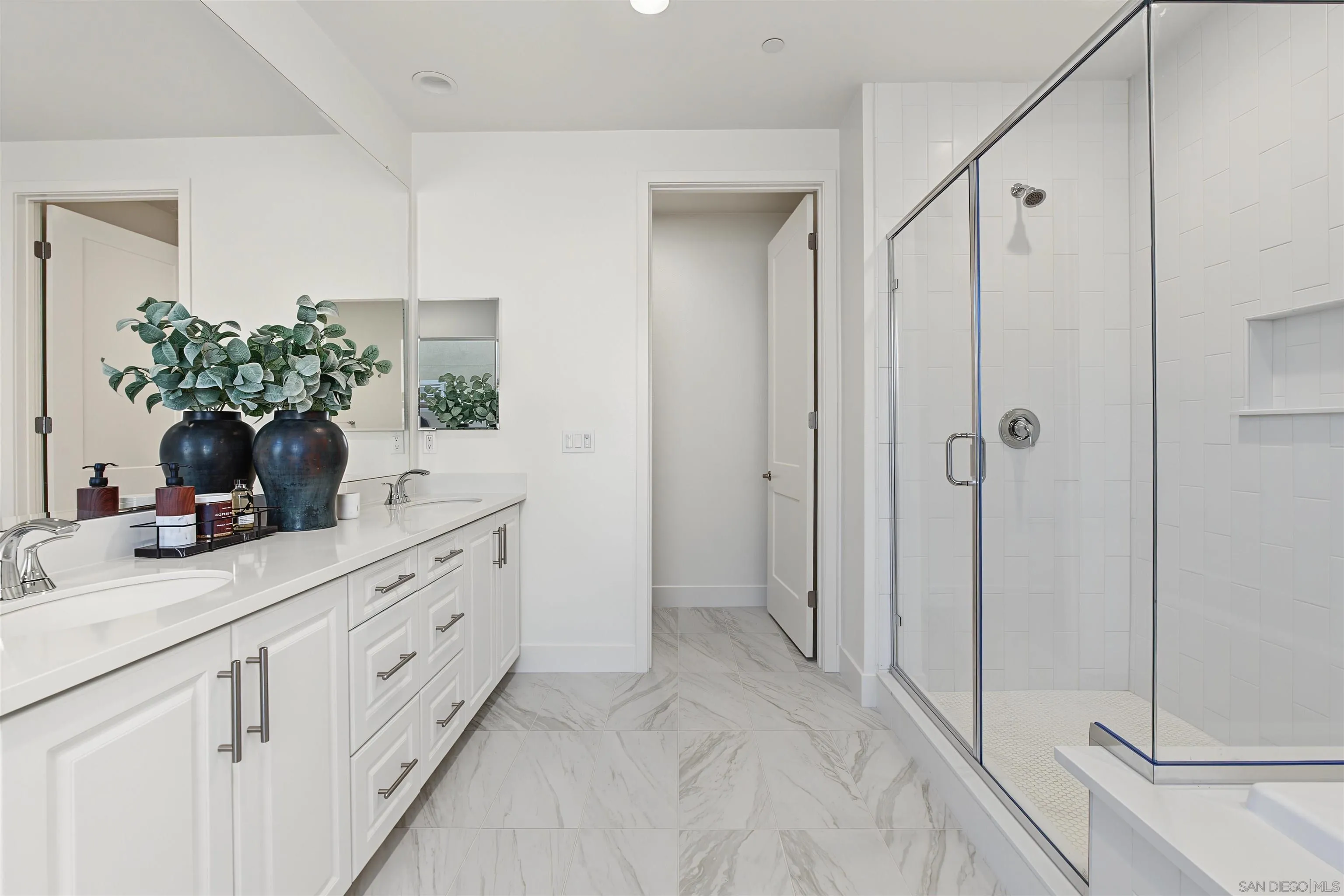 Bathroom with a white double vanity and glass-enclosed, white-tiled shower.