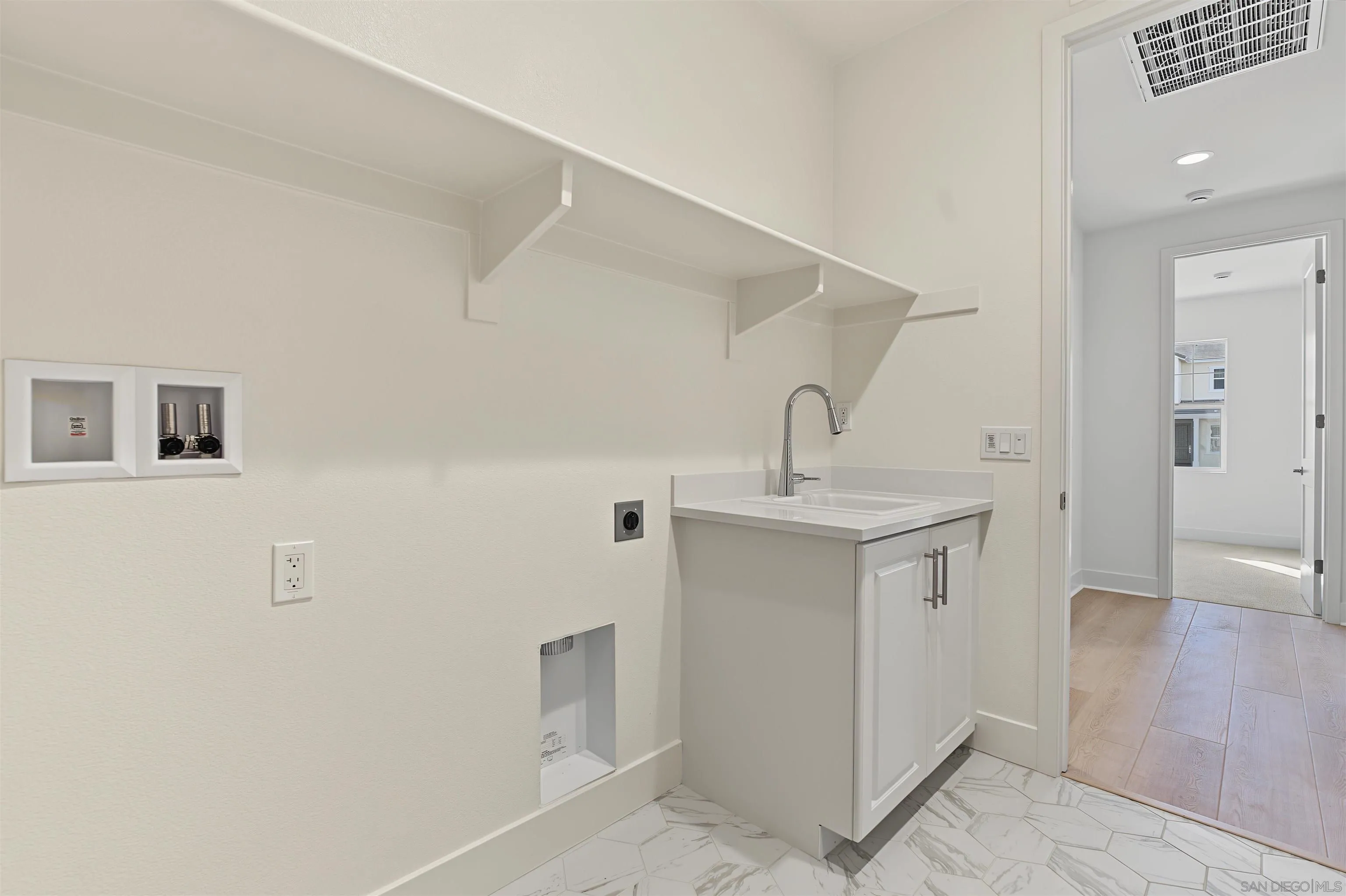 Laundry room with a utility sink, washer hookups, overhead shelf, and patterned tile floor.