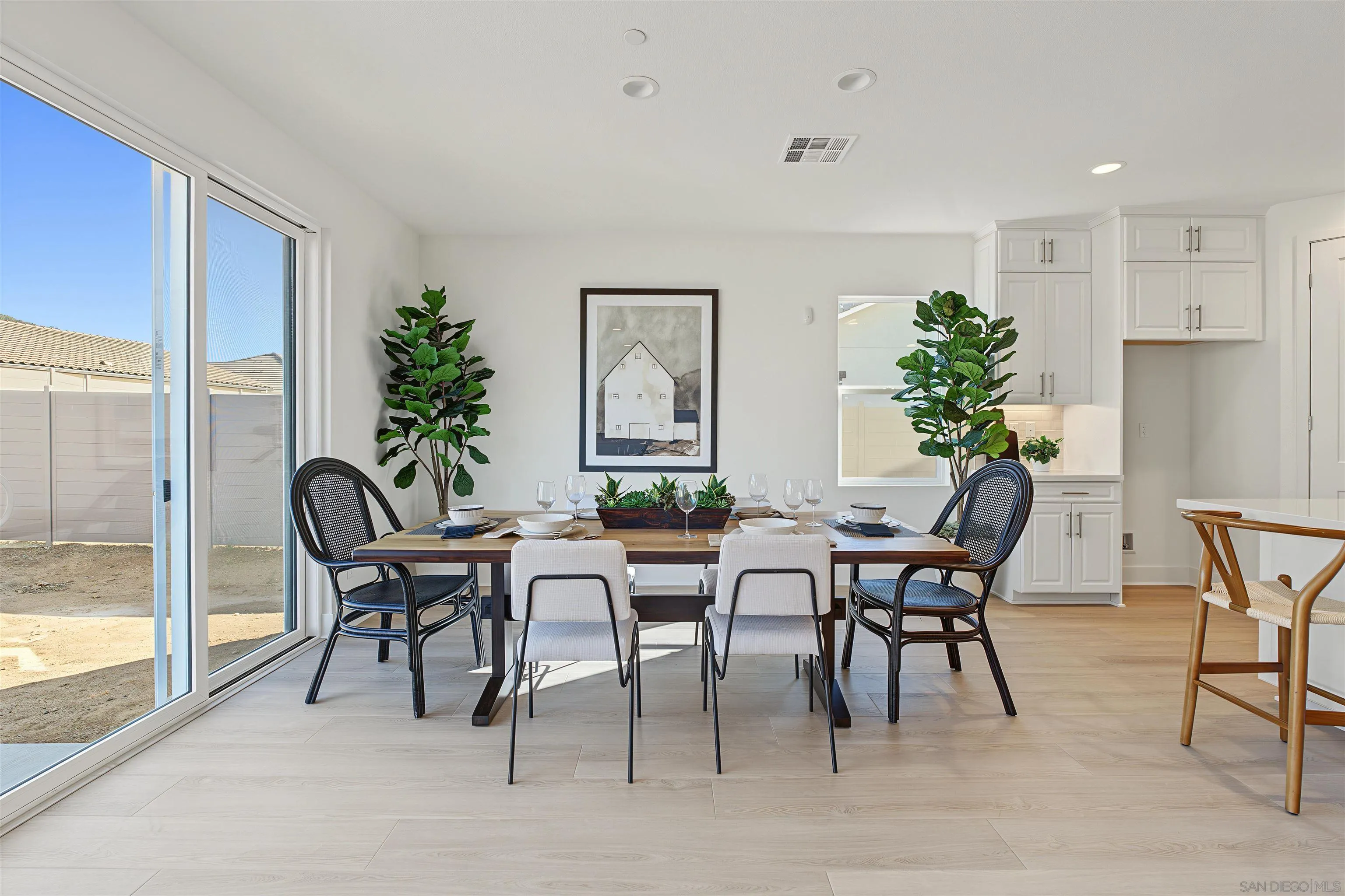 Dining area with a set wood table beside large sliding glass doors and a white kitchen.