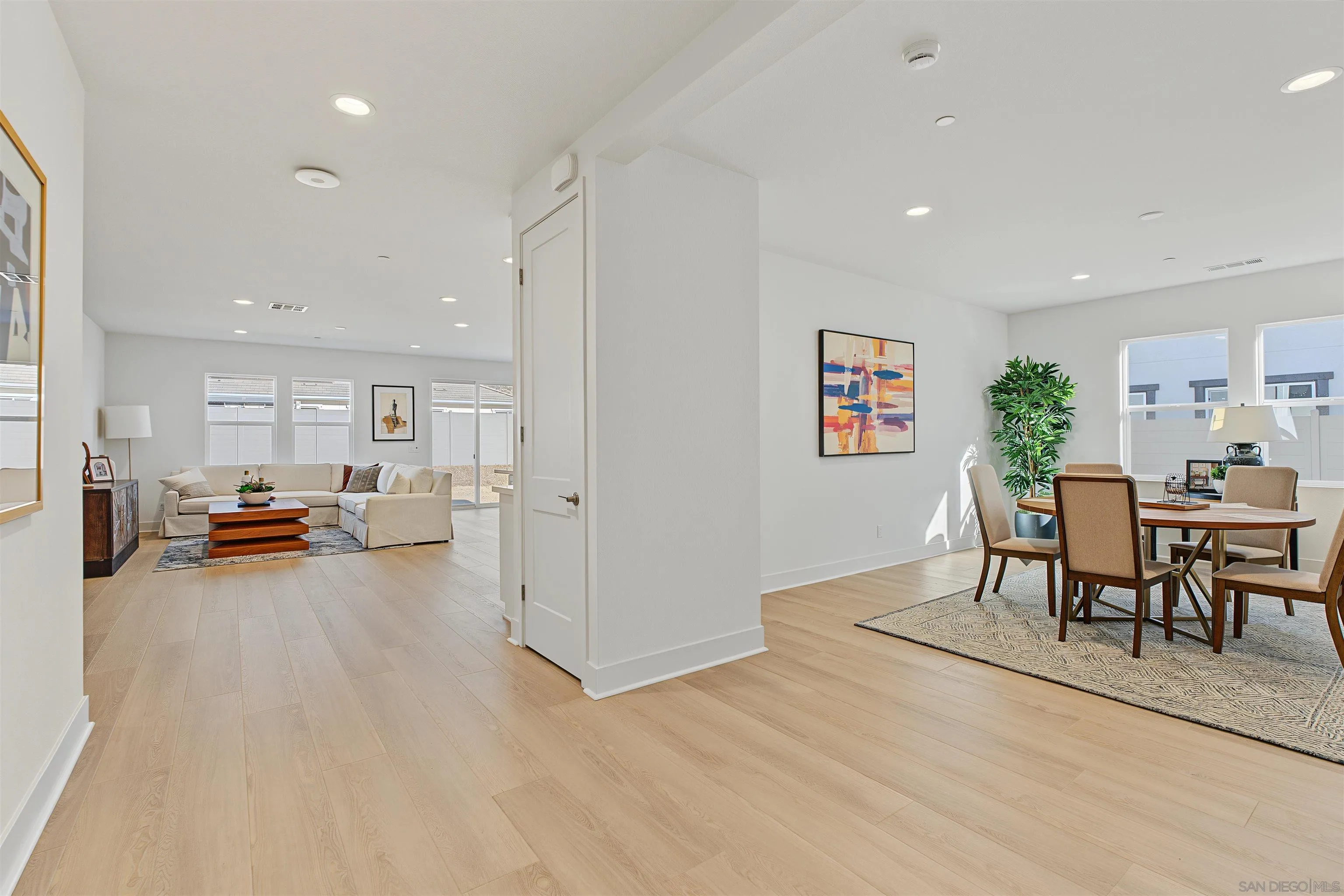 Open-plan living and dining room with a cream sectional, light wood floors, and large windows.