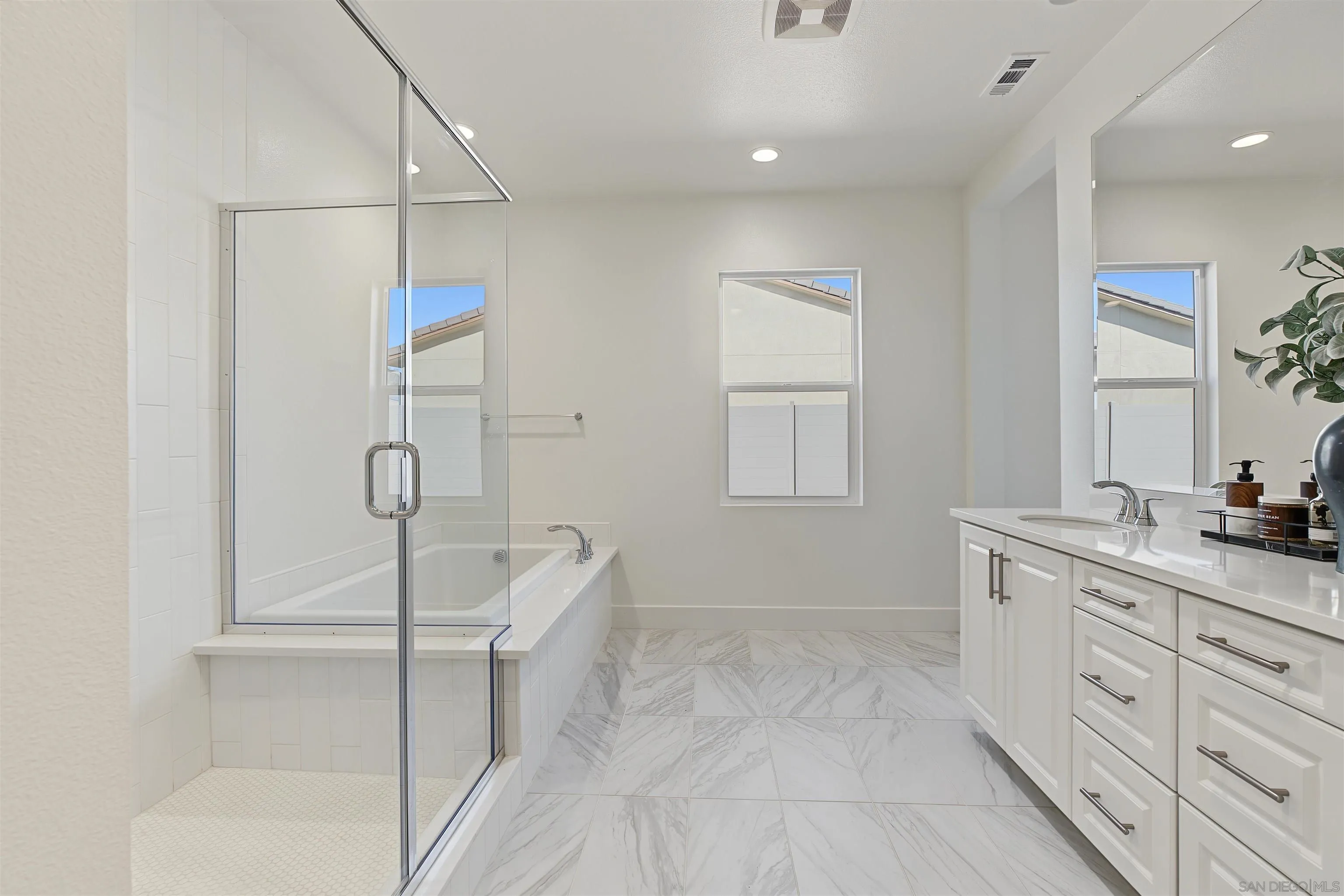 Bright bathroom with a glass shower, built-in tub, double-sink vanity, and marble-look tile floors.
