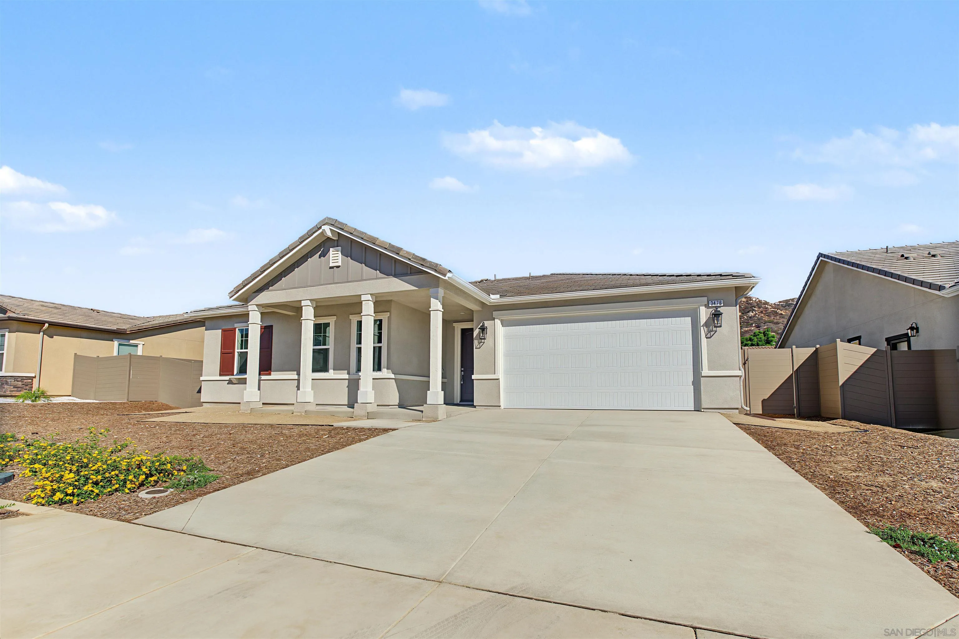 Single-story gray home with a columned porch, white double garage door, and wide concrete driveway.