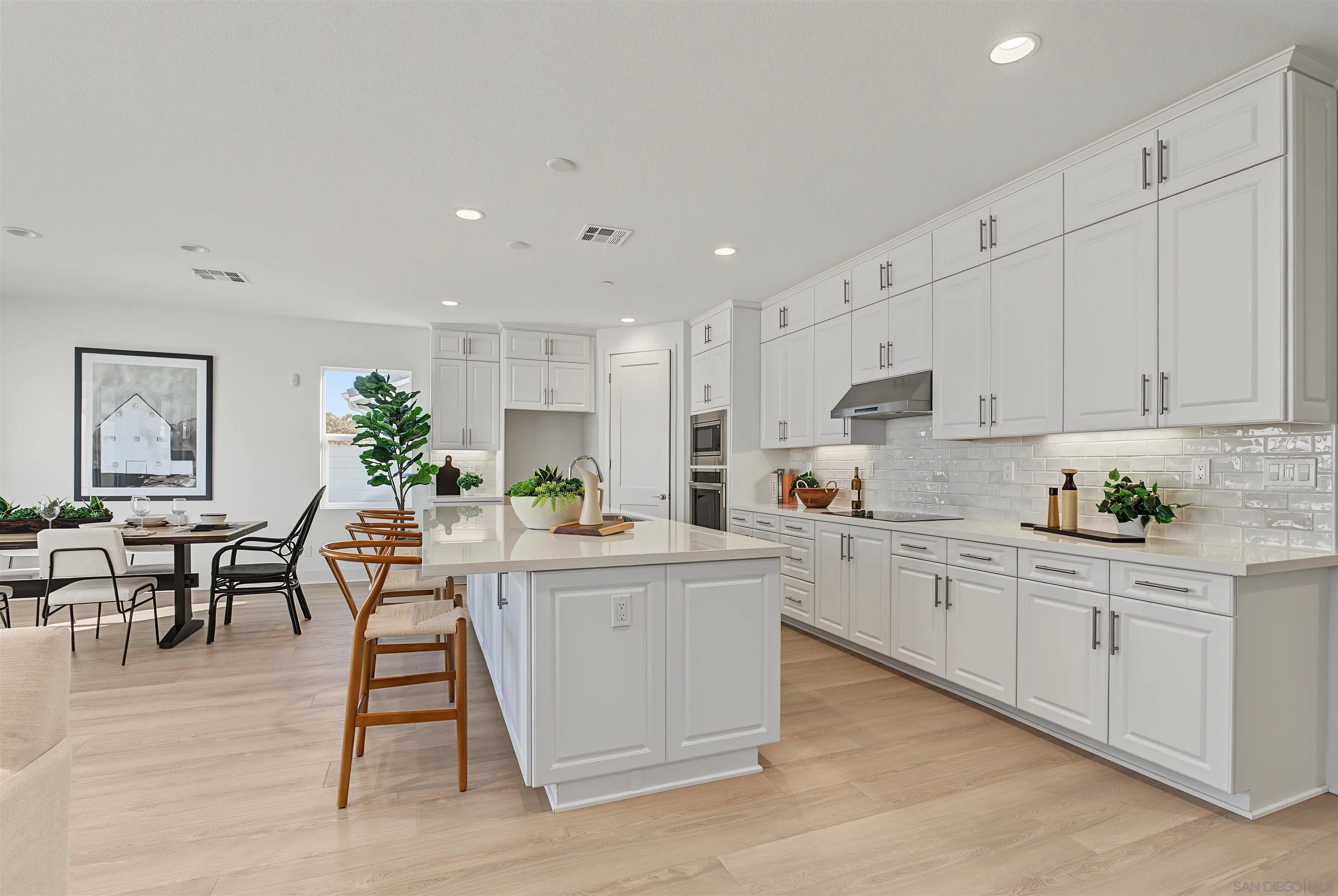 Bright white kitchen with a large island, shaker cabinets, and an adjoining dining area.