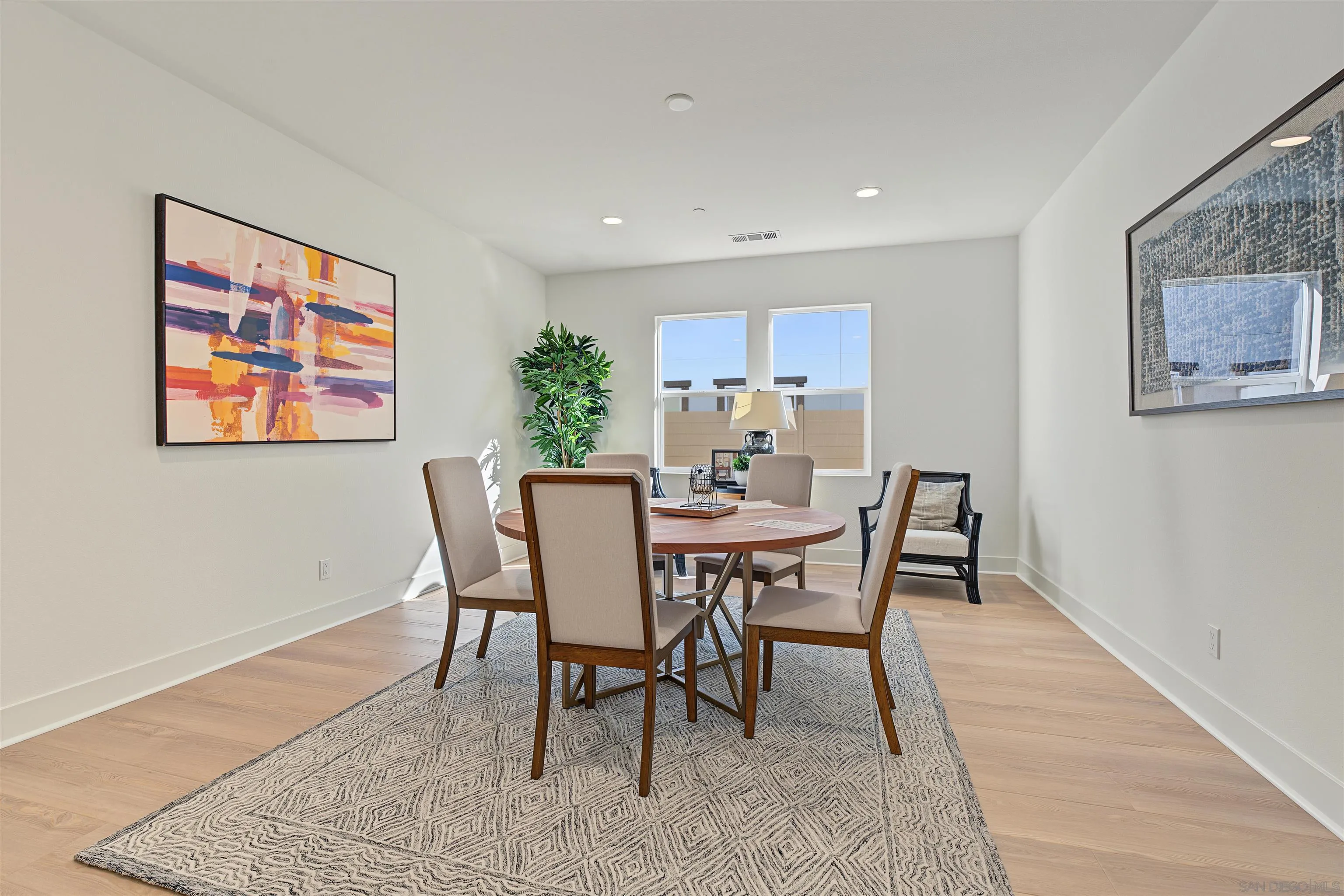 Staged dining room with a round table, upholstered chairs, patterned rug, and abstract wall art.