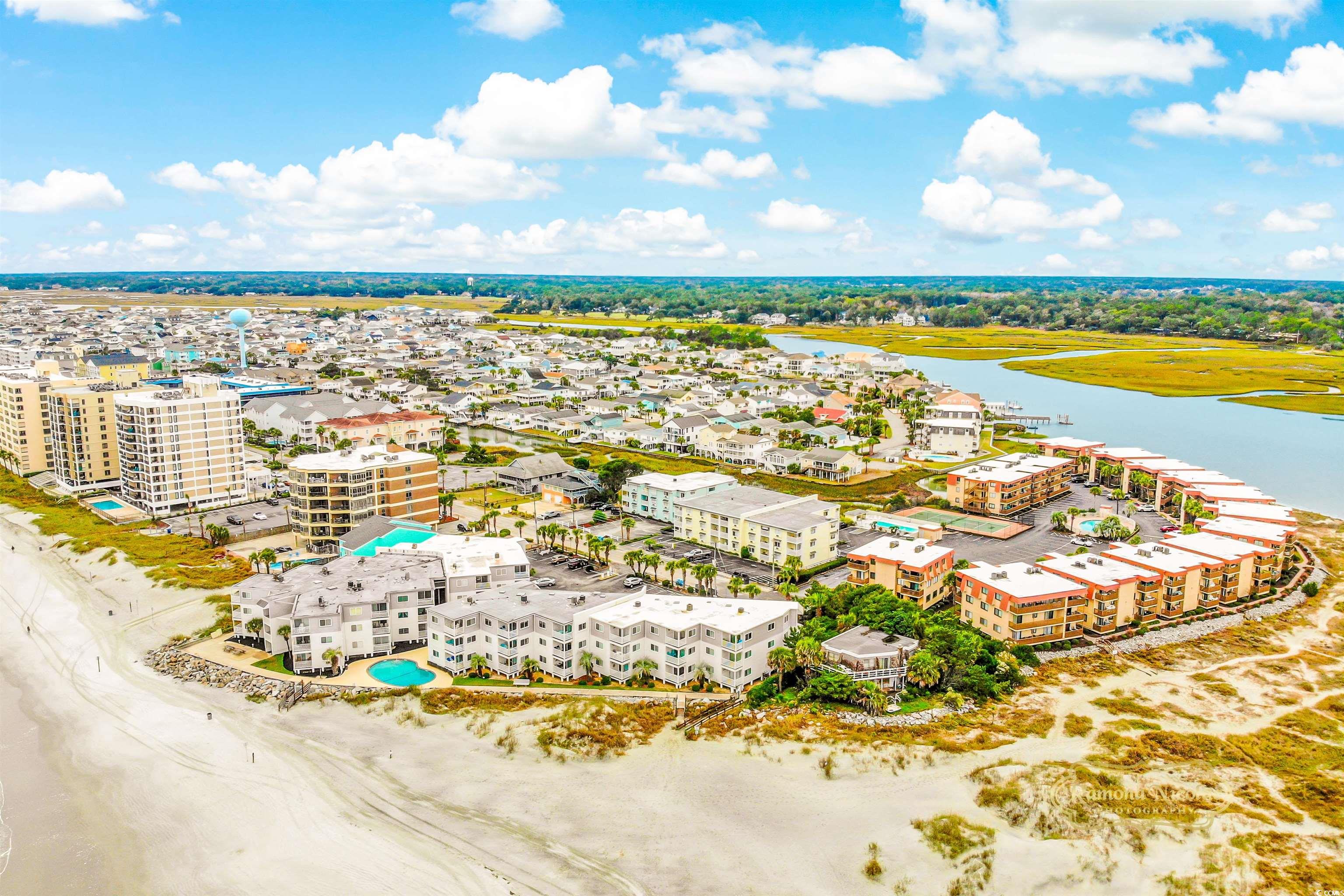 Aerial view of beachfront condominiums beside a sandy beach and marsh-lined inlet.