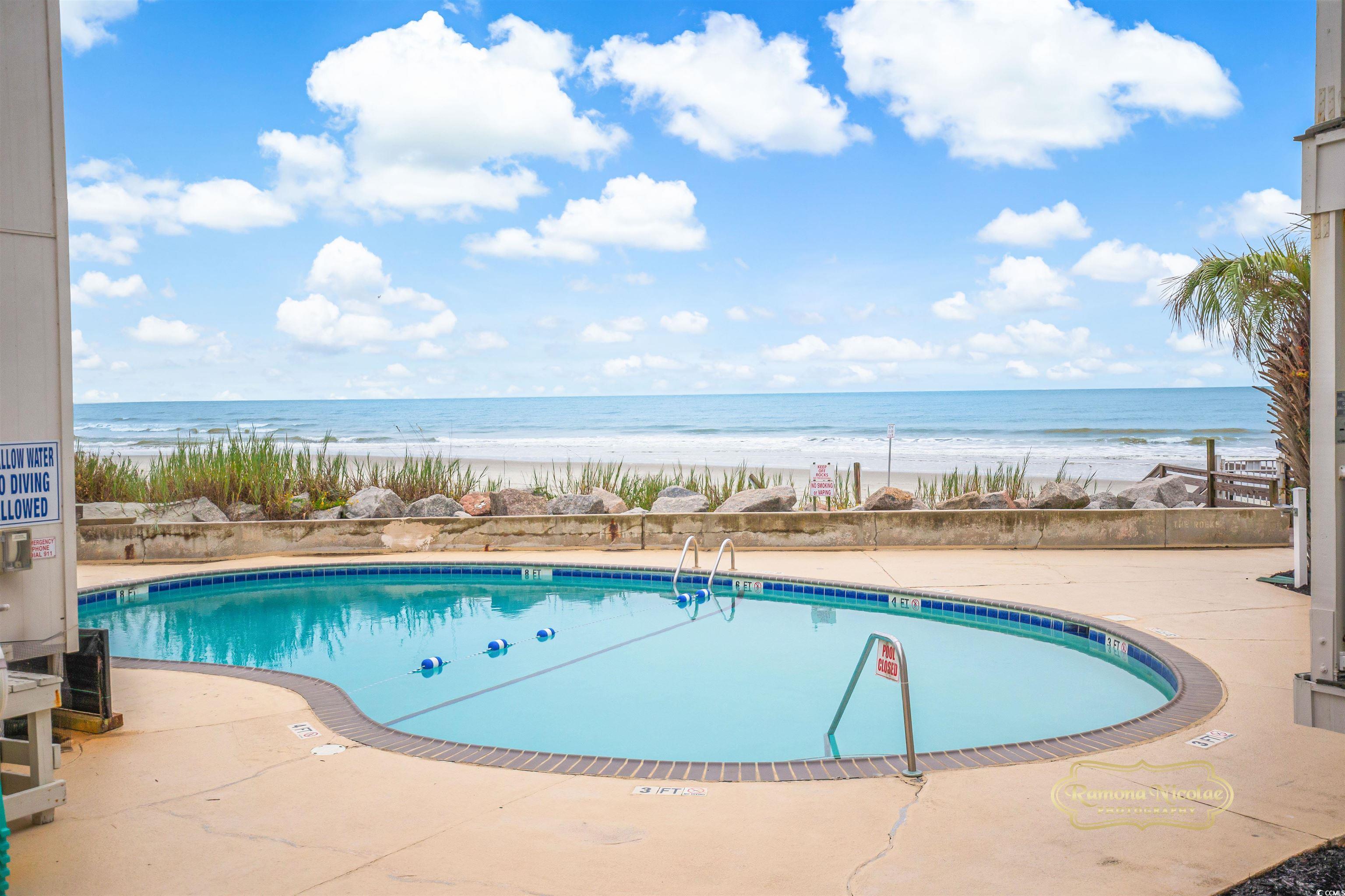 Outdoor swimming pool overlooking the beach and ocean, framed by resort buildings.