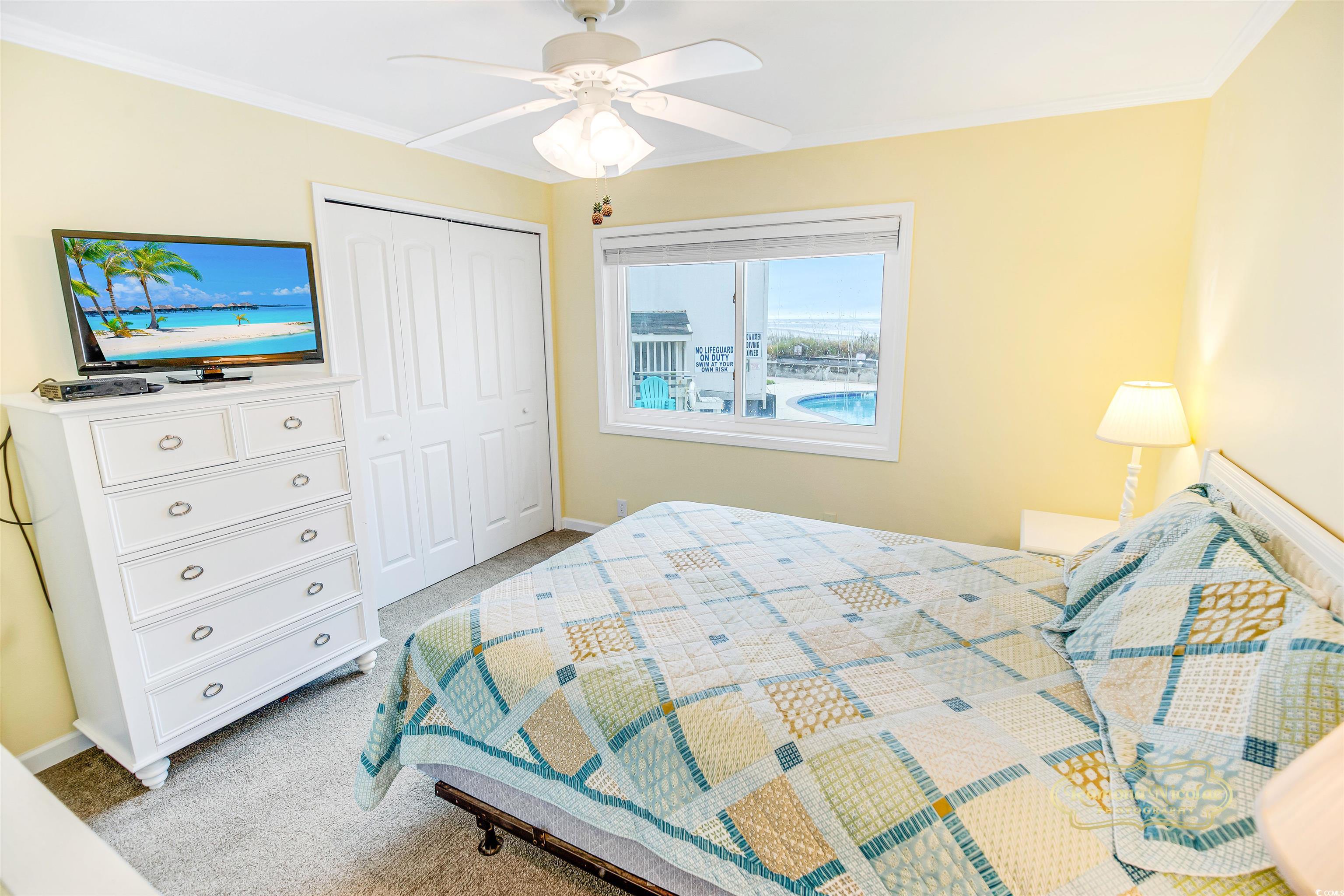 Bedroom with a patchwork quilt, white dresser, and window overlooking a pool and ocean.