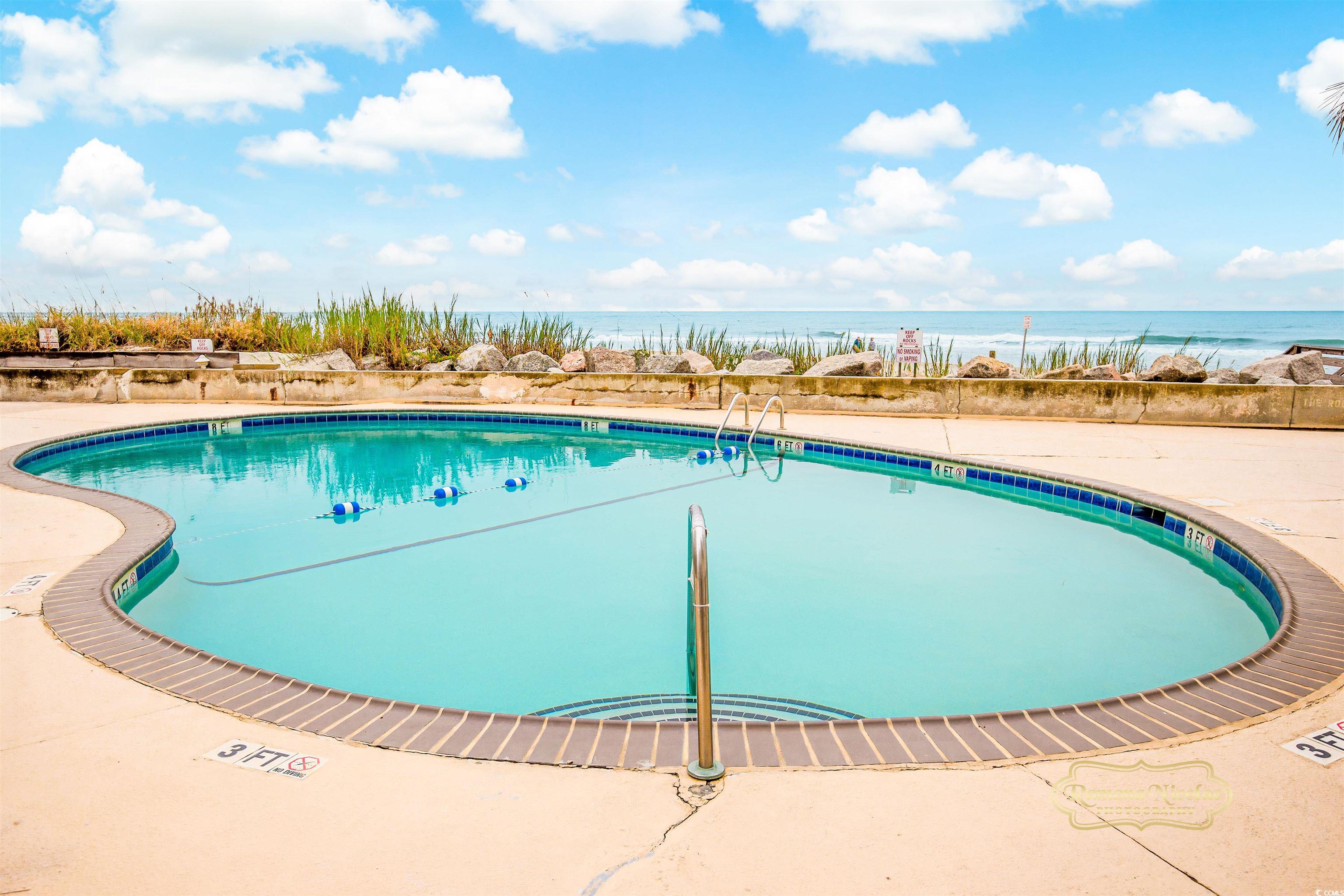 Outdoor swimming pool beside the ocean, with a curved deck and shoreline rocks.