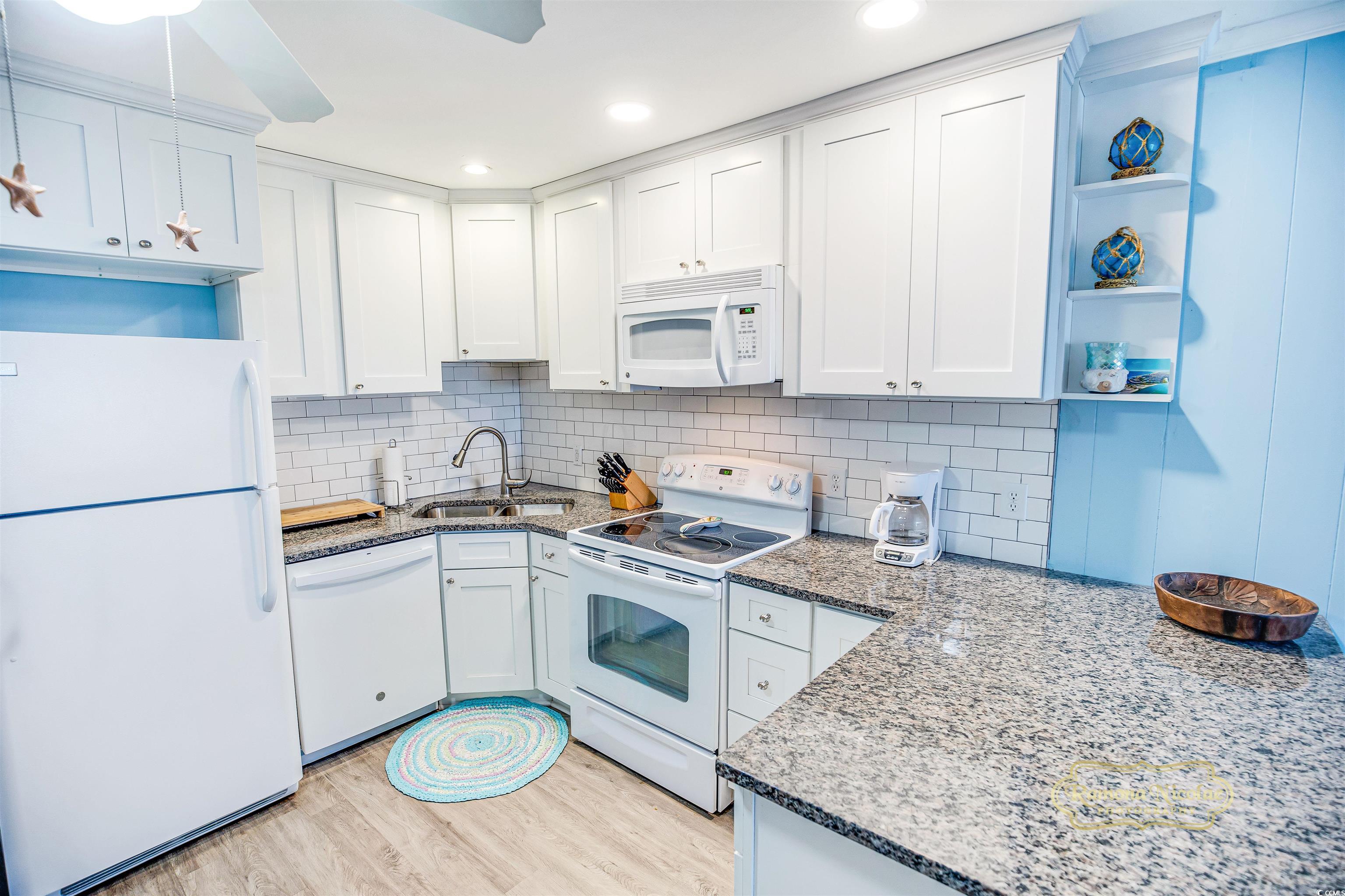 Bright white kitchen with granite counters, subway tile backsplash, and blue display shelves.